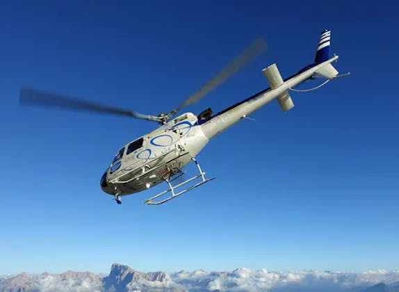 Helikopter vliegt over de Alpen, helder zicht, blauwe lucht.