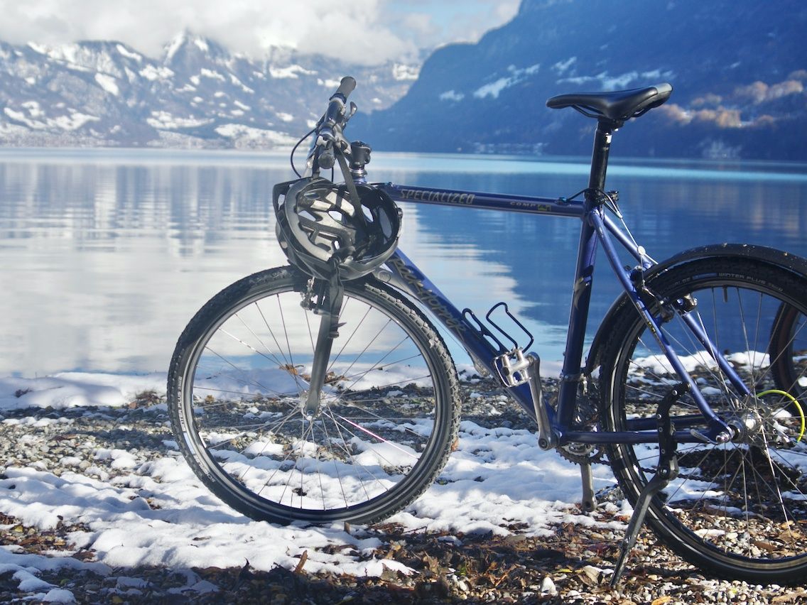 Passeio de bicicleta: bicicleta à beira do lago na paisagem de inverno com margens e montanhas cobertas de neve ao fundo.