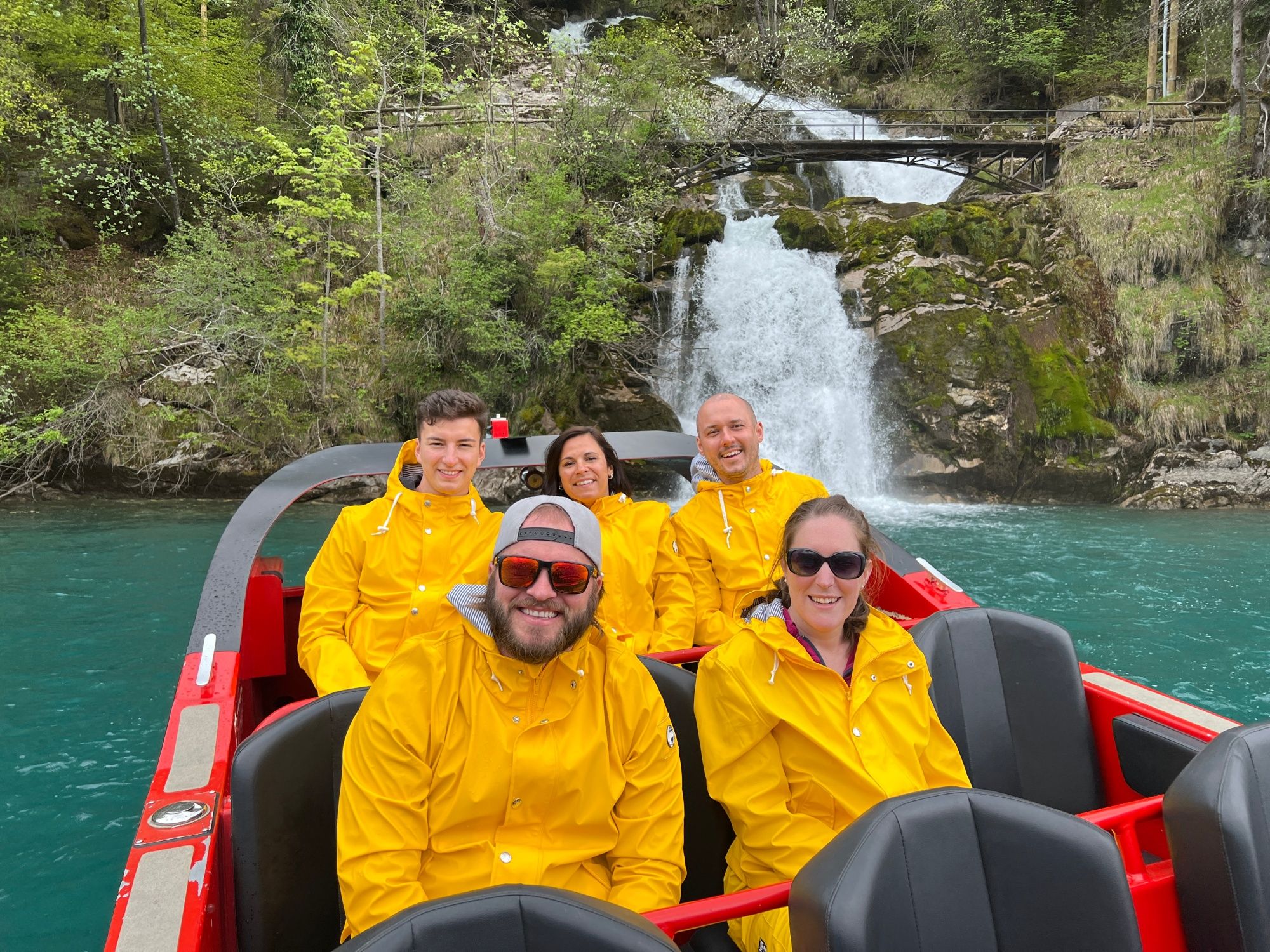Jetbåt på Brienzersee med grupp i gula regnjackor framför vattenfallet
