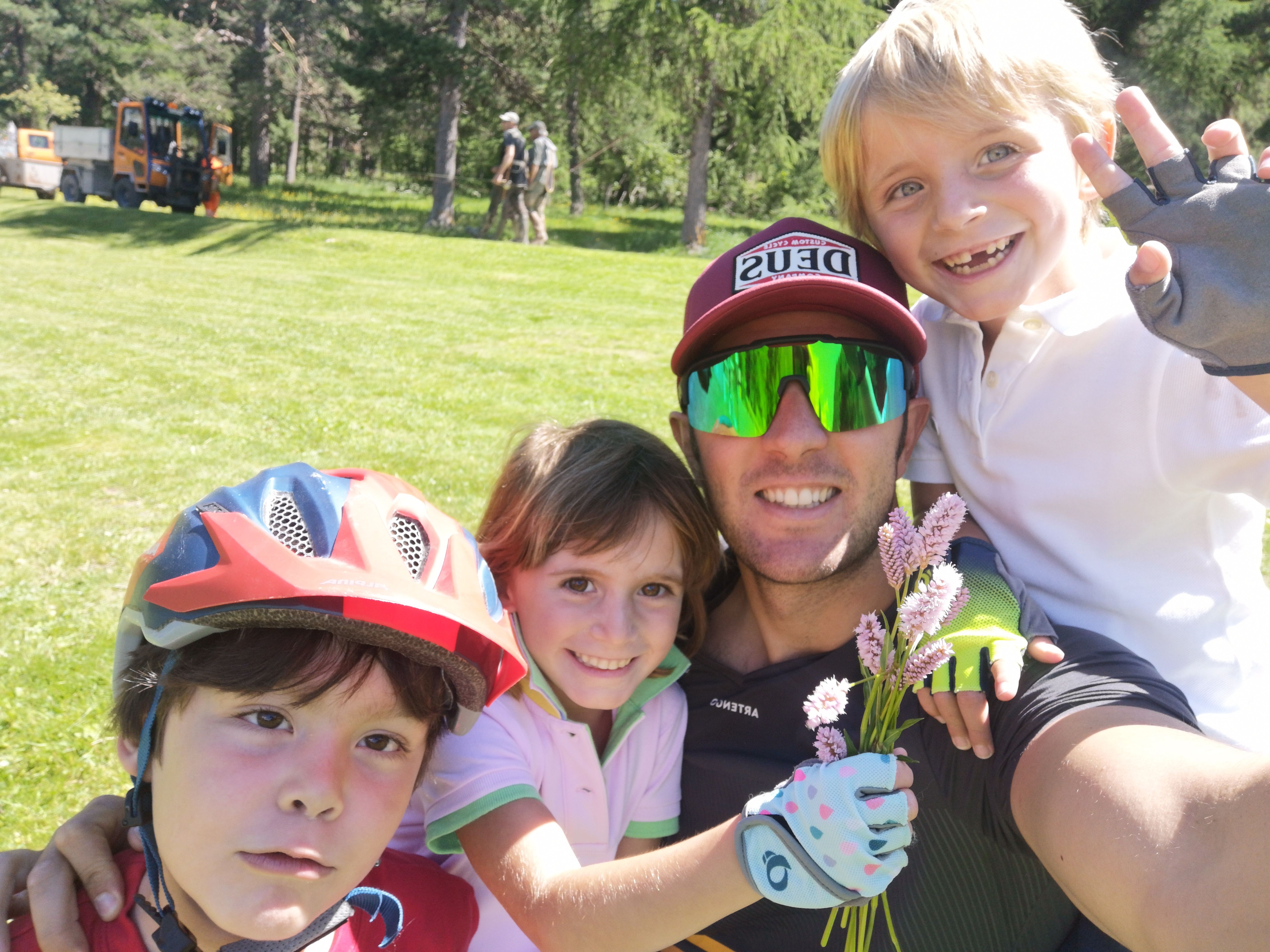 Obóz dla dzieci w St. Moritz: Dzieci uśmiechają się z dorosłym na zewnątrz, w otoczeniu kwiatów i sprzętu sportowego.