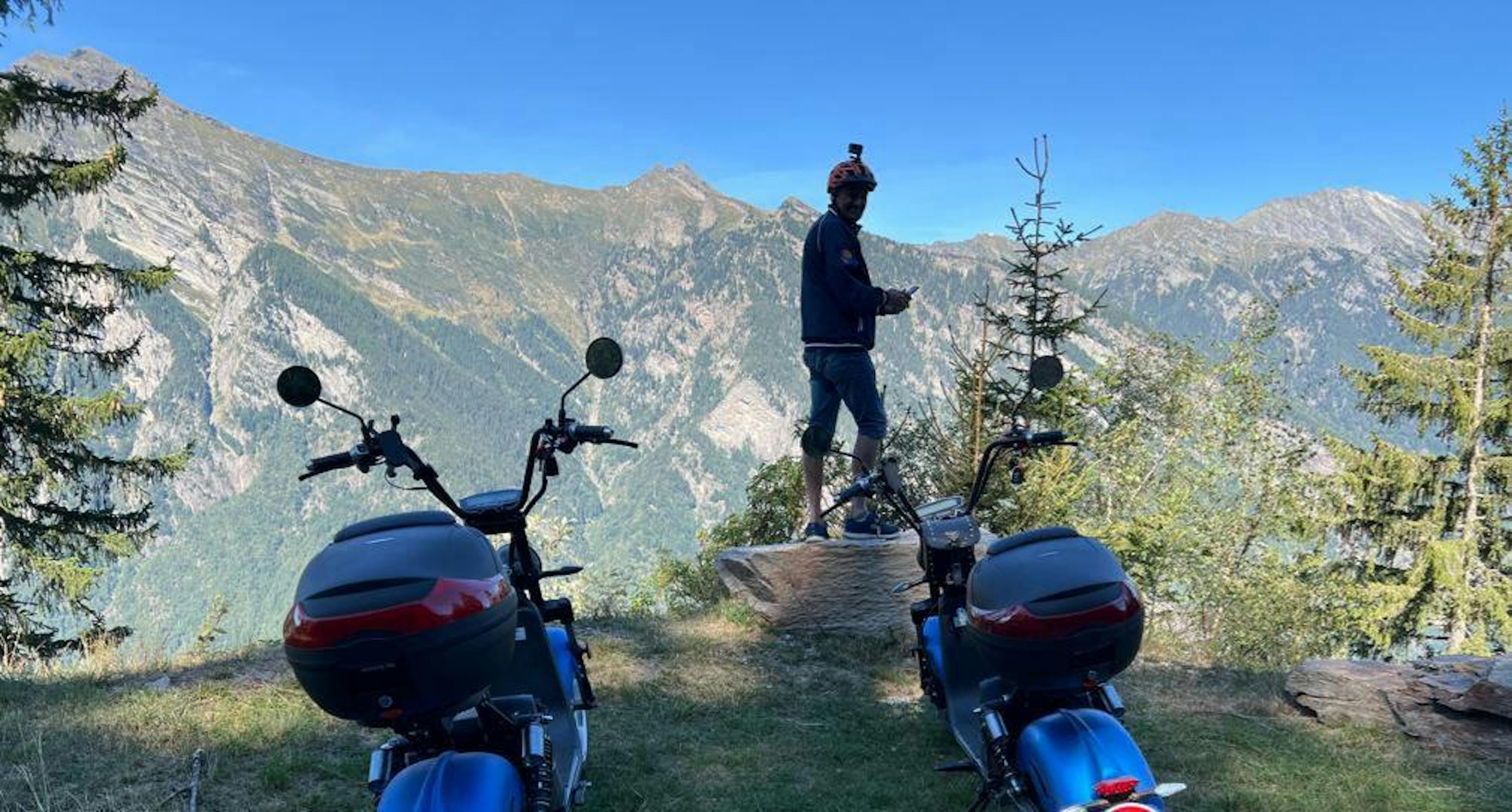 ticinoquad: Мотопутешественник в природе с горными вершинами на заднем плане и квадроциклами.