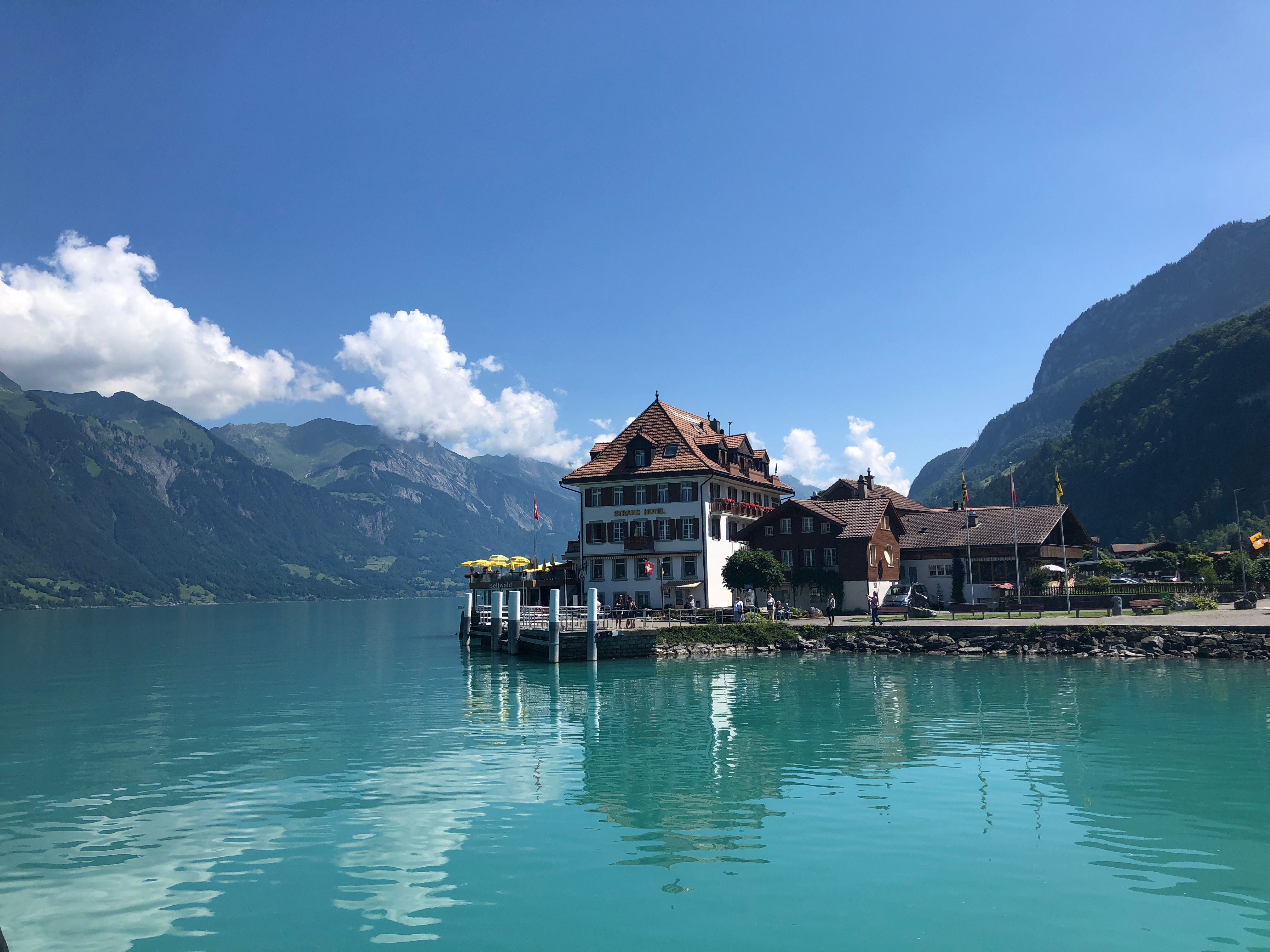 Schifffahrt Brienzersee mit Aussicht auf das Restaurant am Wasser, schöne Berglandschaft, bewölkter Himmel