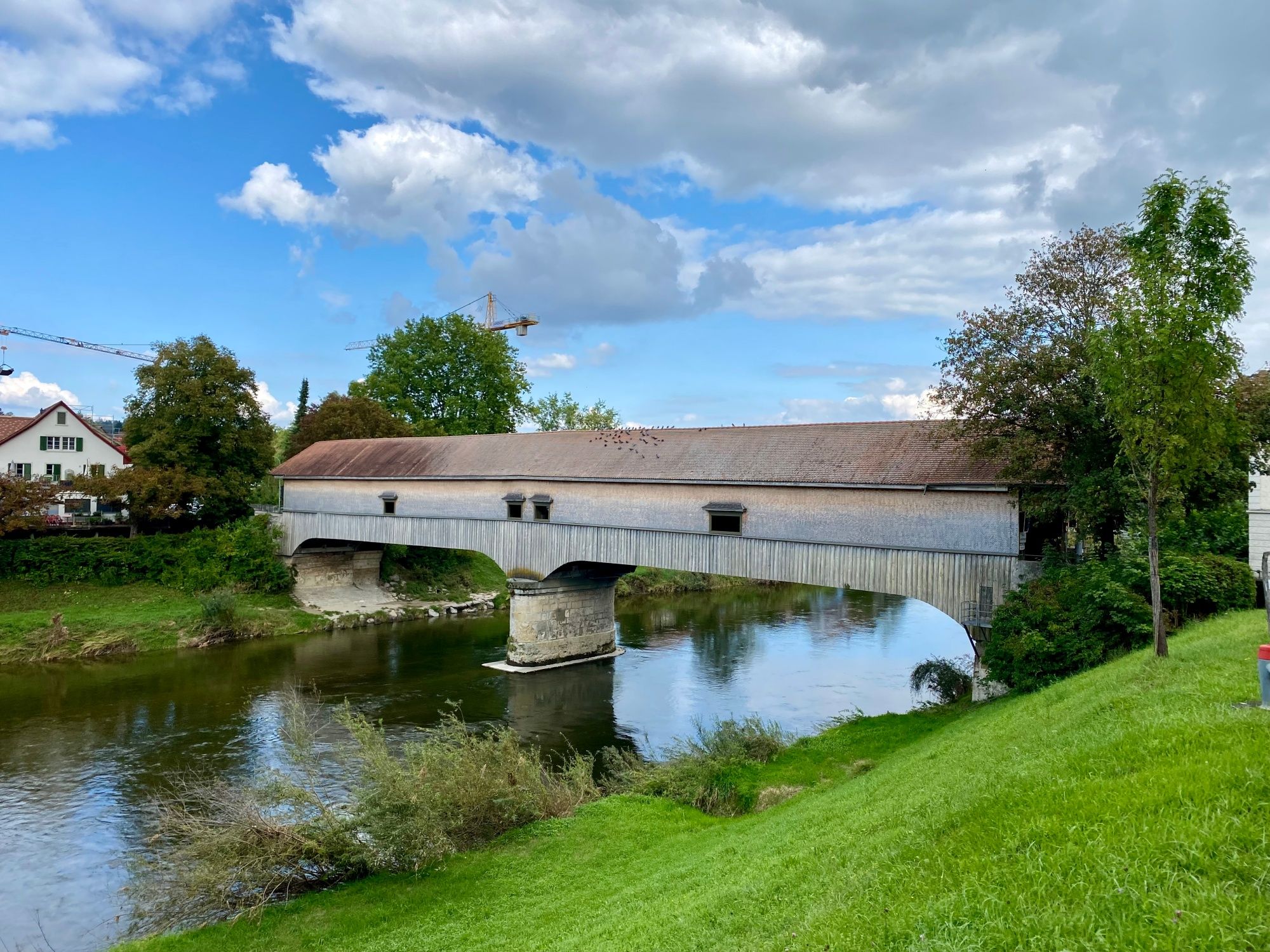 ponte coberta sobre o rio com áreas verdes e nuvens no céu, ideal para amantes da natureza.