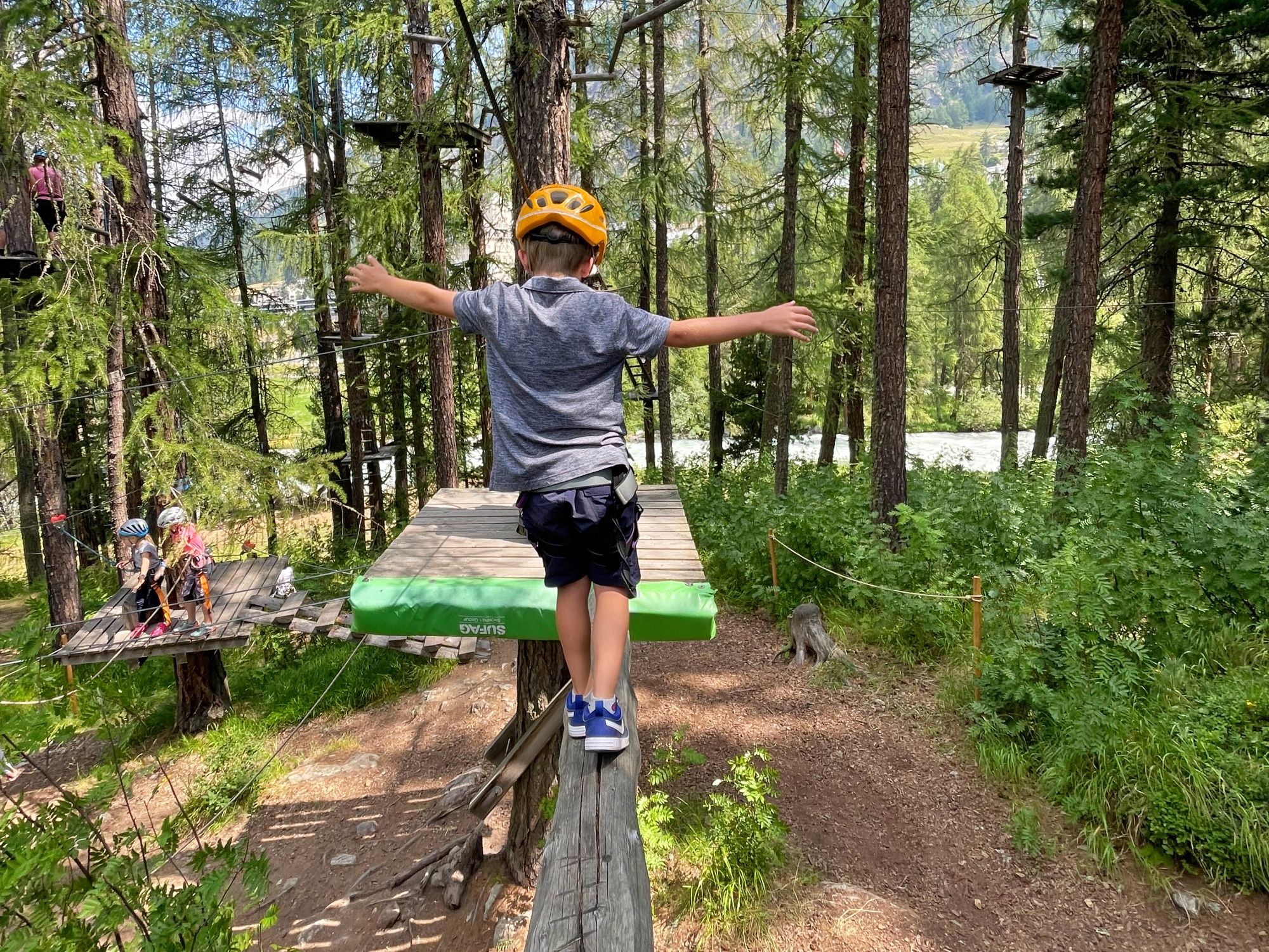 Obóz dla dzieci: dzieci przeżywają przygody na łonie natury w St. Moritz, na platformie na wysokości drabinki linowej.