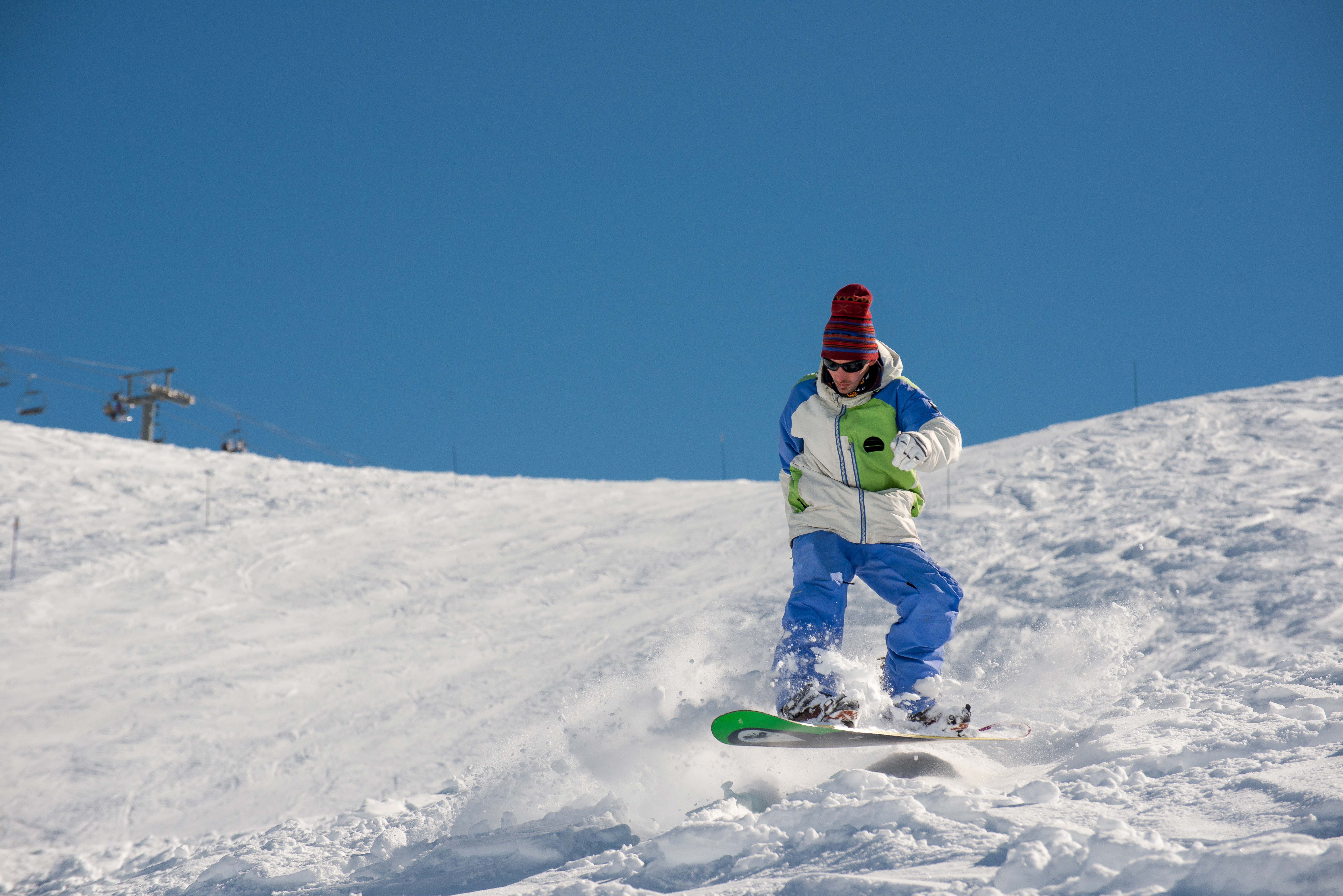 Snowboarder scivola con slancio sulla pista in inverno con sole.