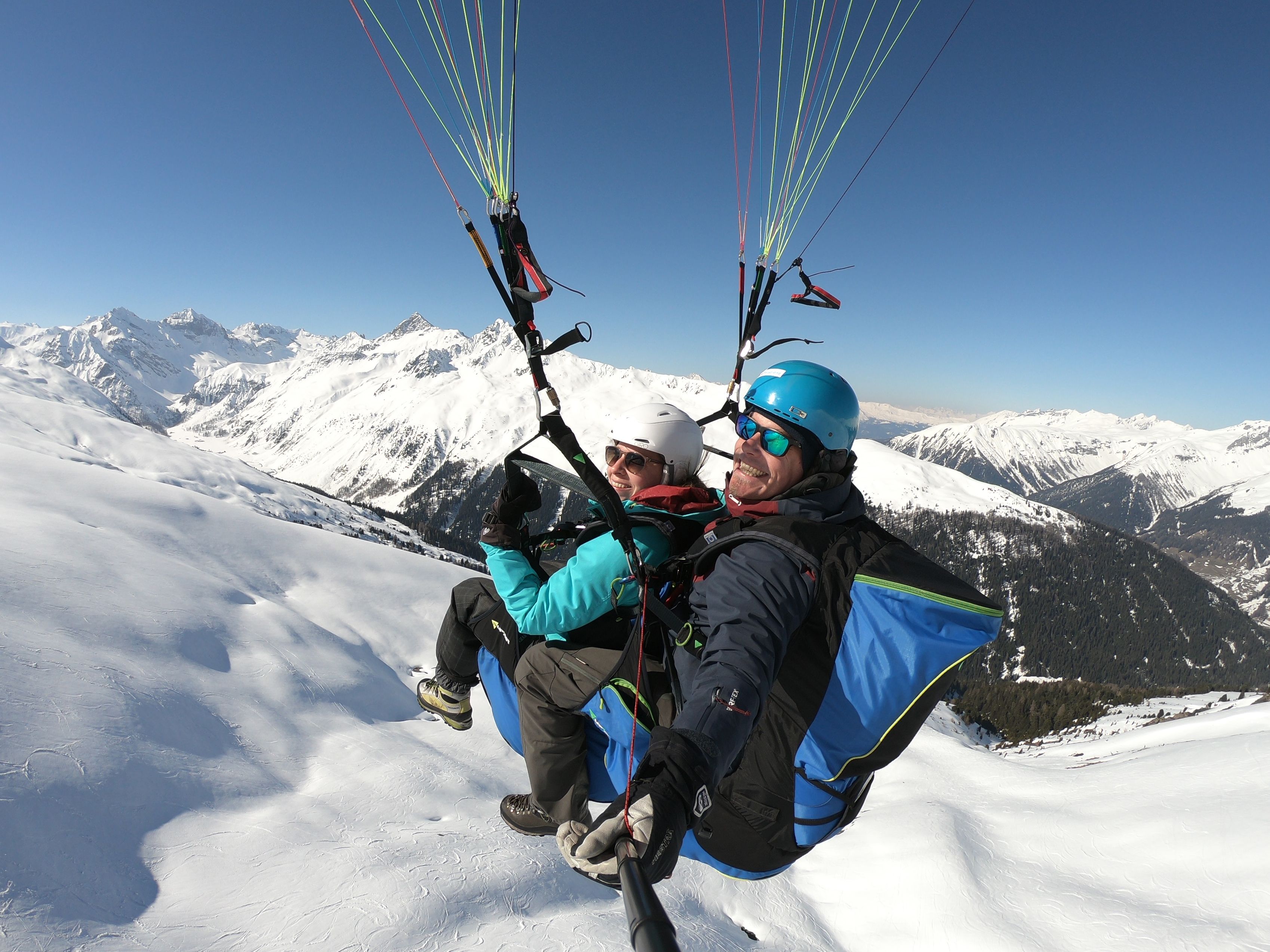 Paragliding Davos se dvěma osobami v teplém oblečení nad zasněženými horami