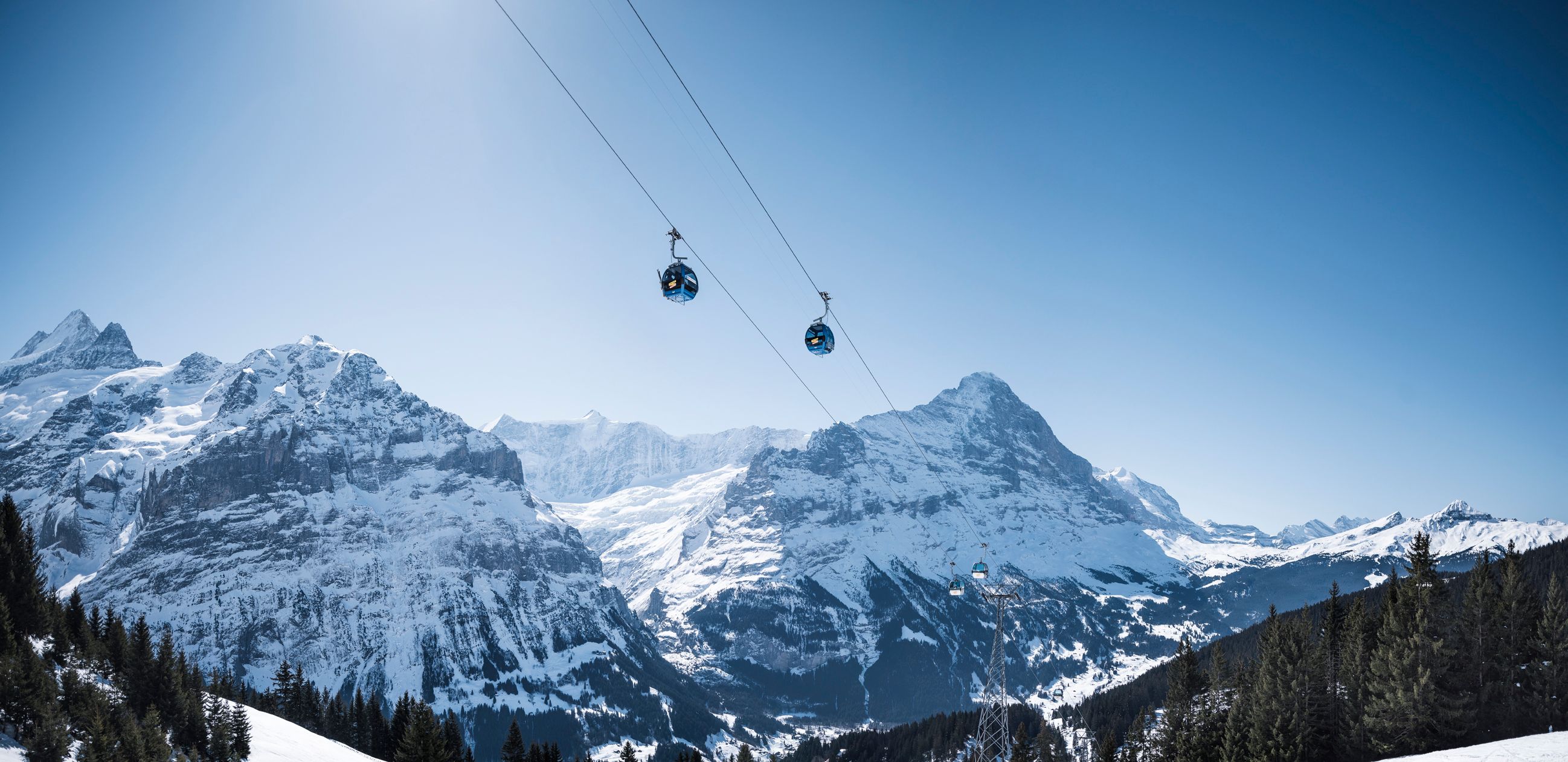융프라우를 향하는 케이블카: 겨울에 그린델발트의 눈 덮인 산 위로 떠 있는 곤돌라의 이미지.