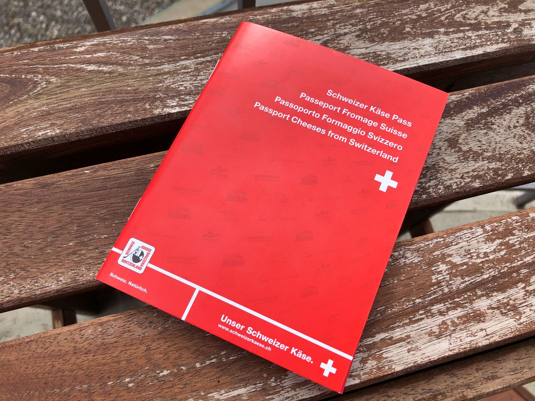 Schweizer Käse Pass zeigt verschiedene Käsesorten. Roter Pass mit Schweizer Kreuz und Beschreibungen. Sichtbar auf Holzuntergrund.