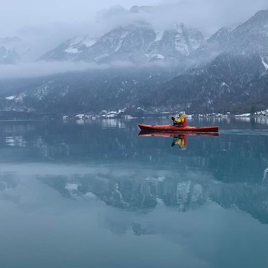 Brienzersee mit Kajakfahrer in winterlicher Landschaft, Berge und Schnee reflektieren im Wasser.