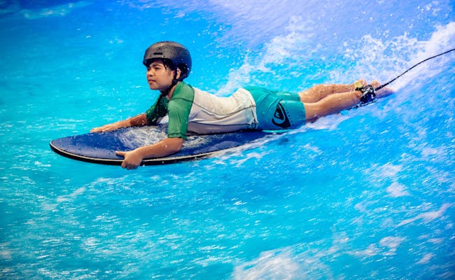 Kids Wave: Kind surft auf Welle in Indoor-Surfanlage.