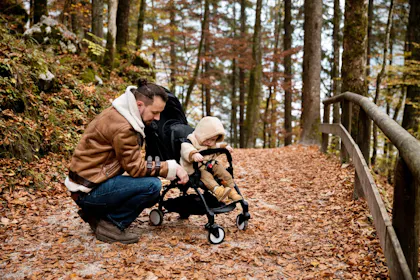 Kinderwagen: Vater zeigt seinem Kind die Natur im Wald, umgeben von buntem Herbstlaub.