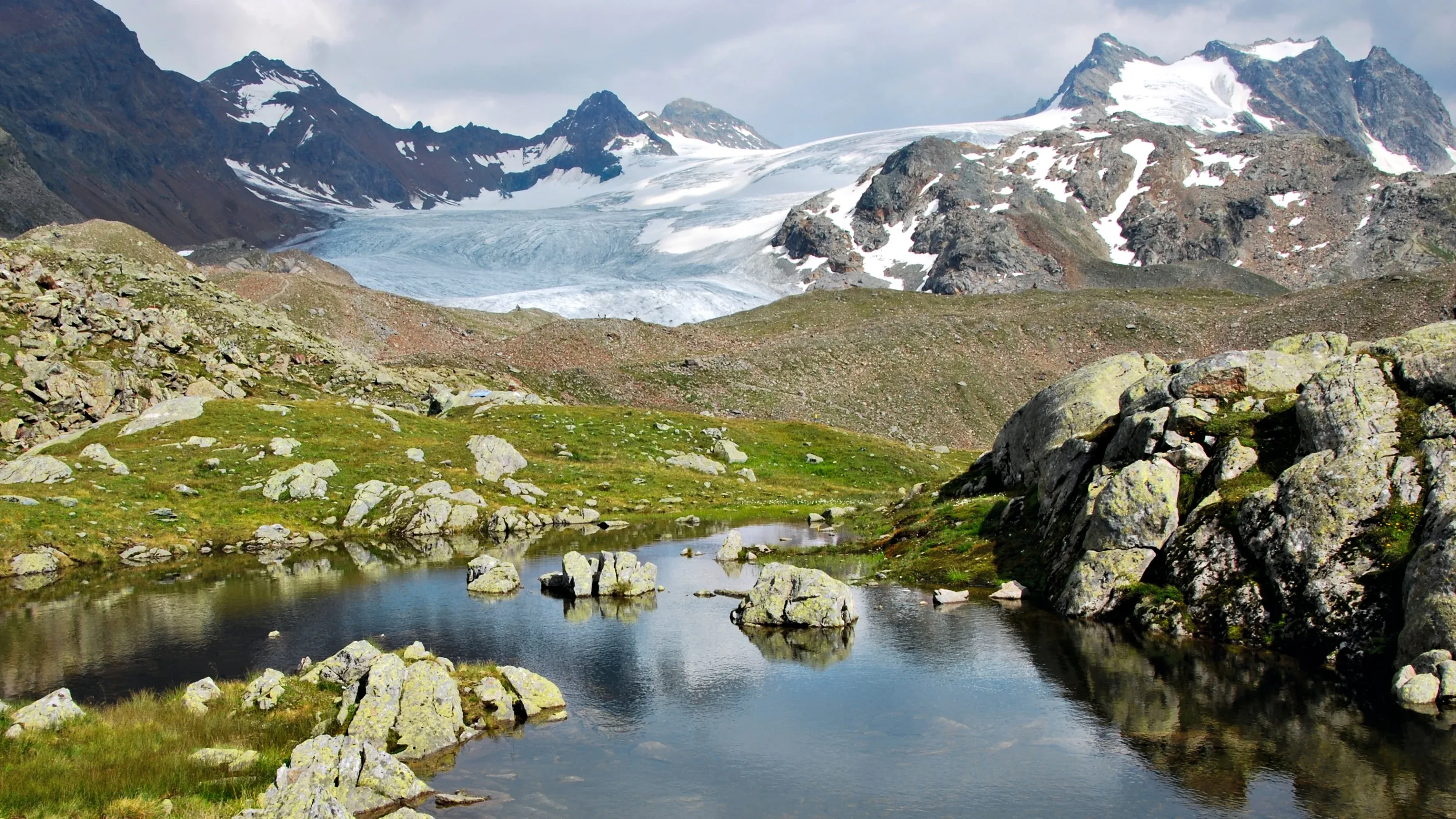 Gletser di latar belakang Klosters, padang rumput alpine, permukaan air jernih.