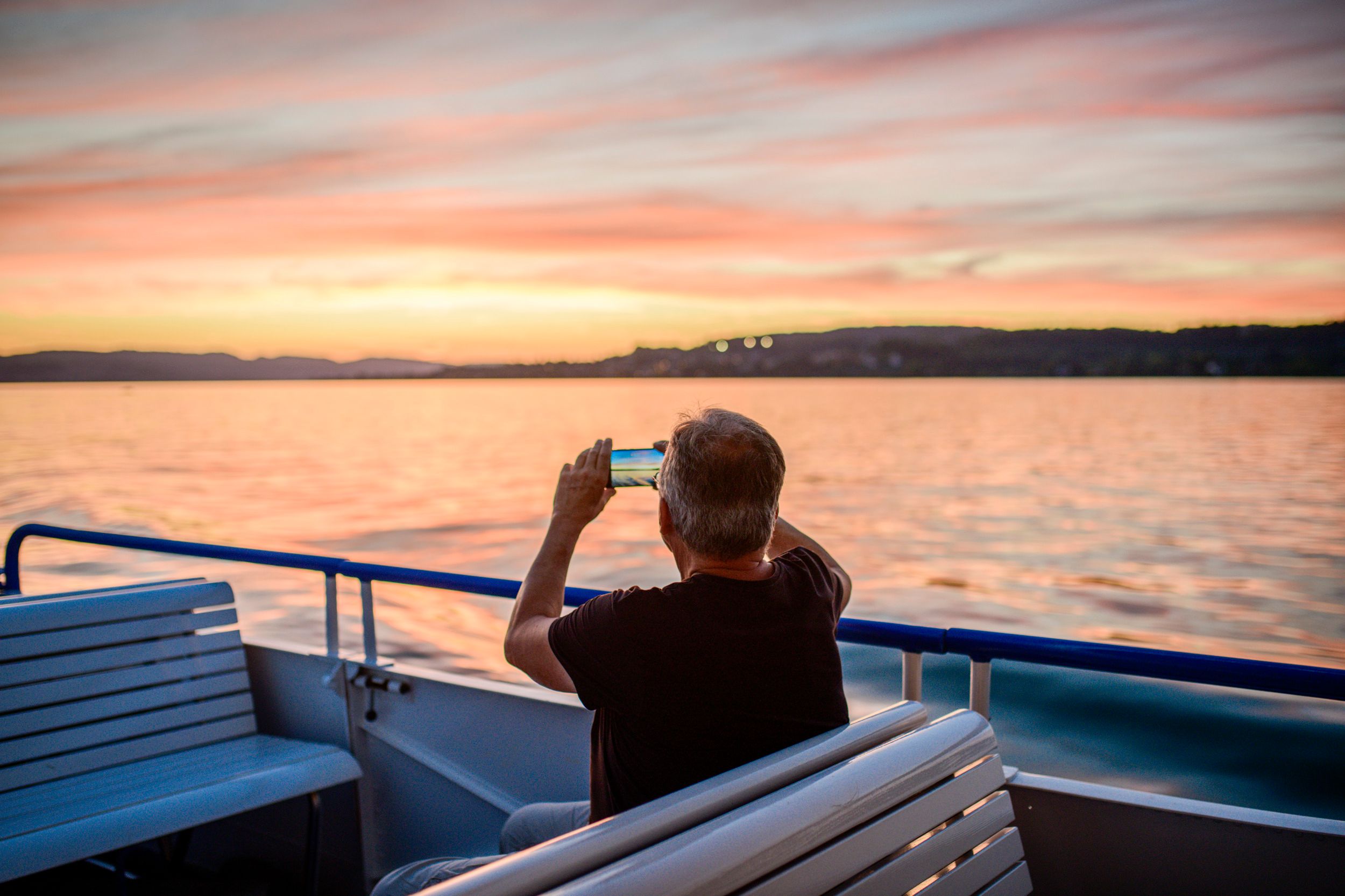 Ufenau: Hombre fotografa la puesta de sol sobre el lago de Zúrich, paisaje pintoresco con vista a Rapperswil