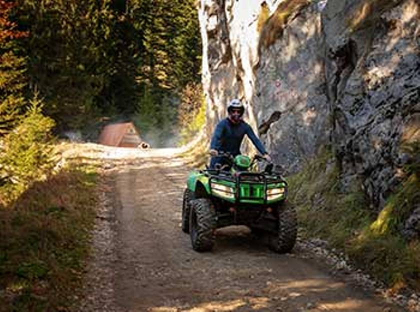 Quad Tour auf einem Waldweg in Baden-Württemberg, Fahrer mit Helm und grüner ATV. Herbstliche Umgebung mit Felsen.