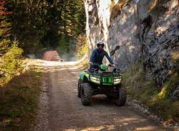 Квадроцикл по лесной дороге в Баден-Вюртемберге, водитель в шлеме и зеленом квадроцикле. Осенняя сцена с скалами.