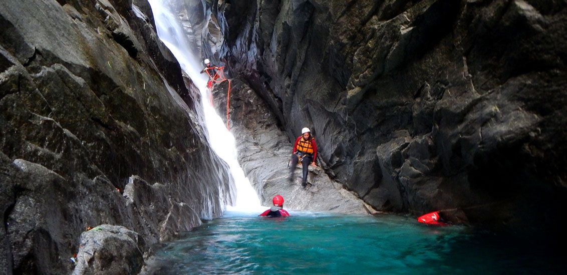 Canyoning Morge w zapierającej dech w piersiach wąwozie z wodospadem i uczestnikami wspinającymi się po skałach.