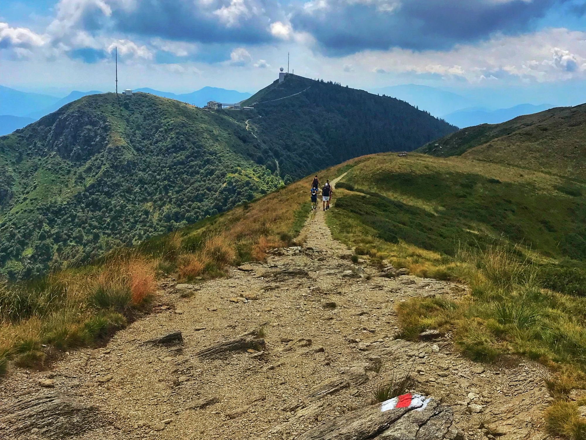 Lemamountain : un groupe marche sur un sentier à travers la nature avec vue sur les montagnes en été.