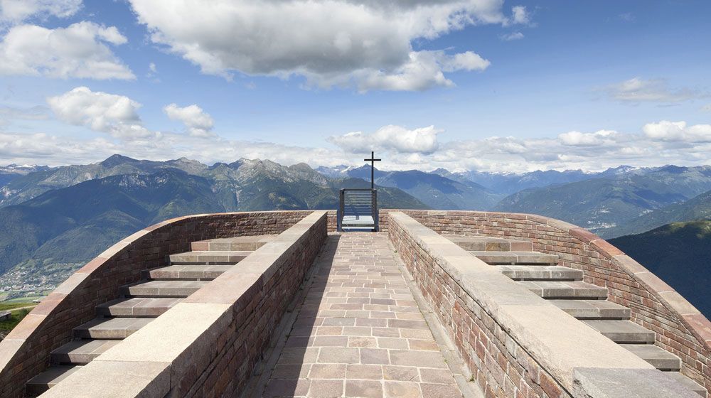 Utsiktsplatsen på Monte Tamaro med stentrappor och kors, omgiven av berg och landskap