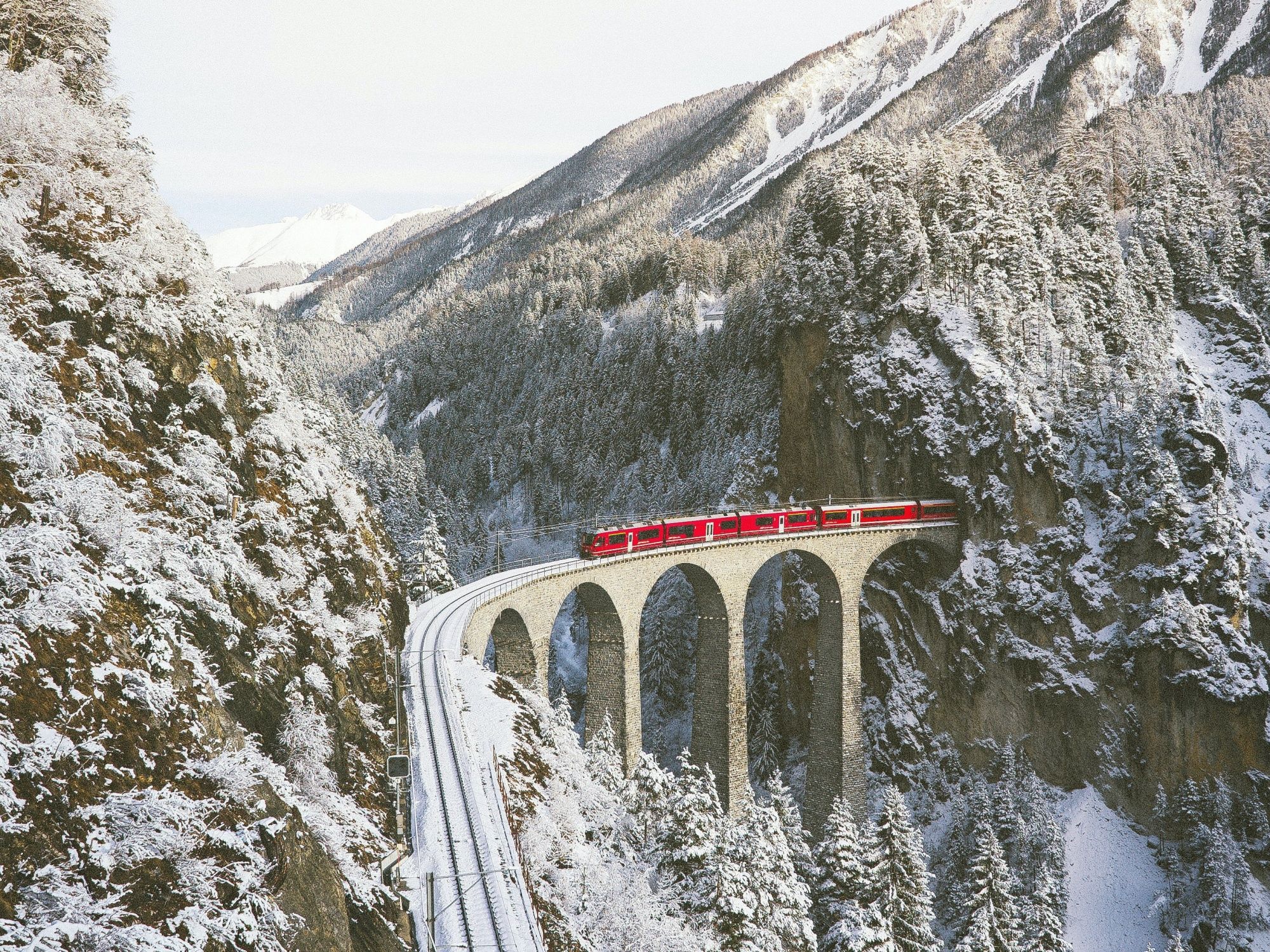 Landwasserviadukt in inverno con montagne coperte di neve e un treno rosso, impressionante scenario naturale.