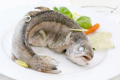 Trout Gstaad di atas piring, dihiasi sayuran dan jeruk nipis