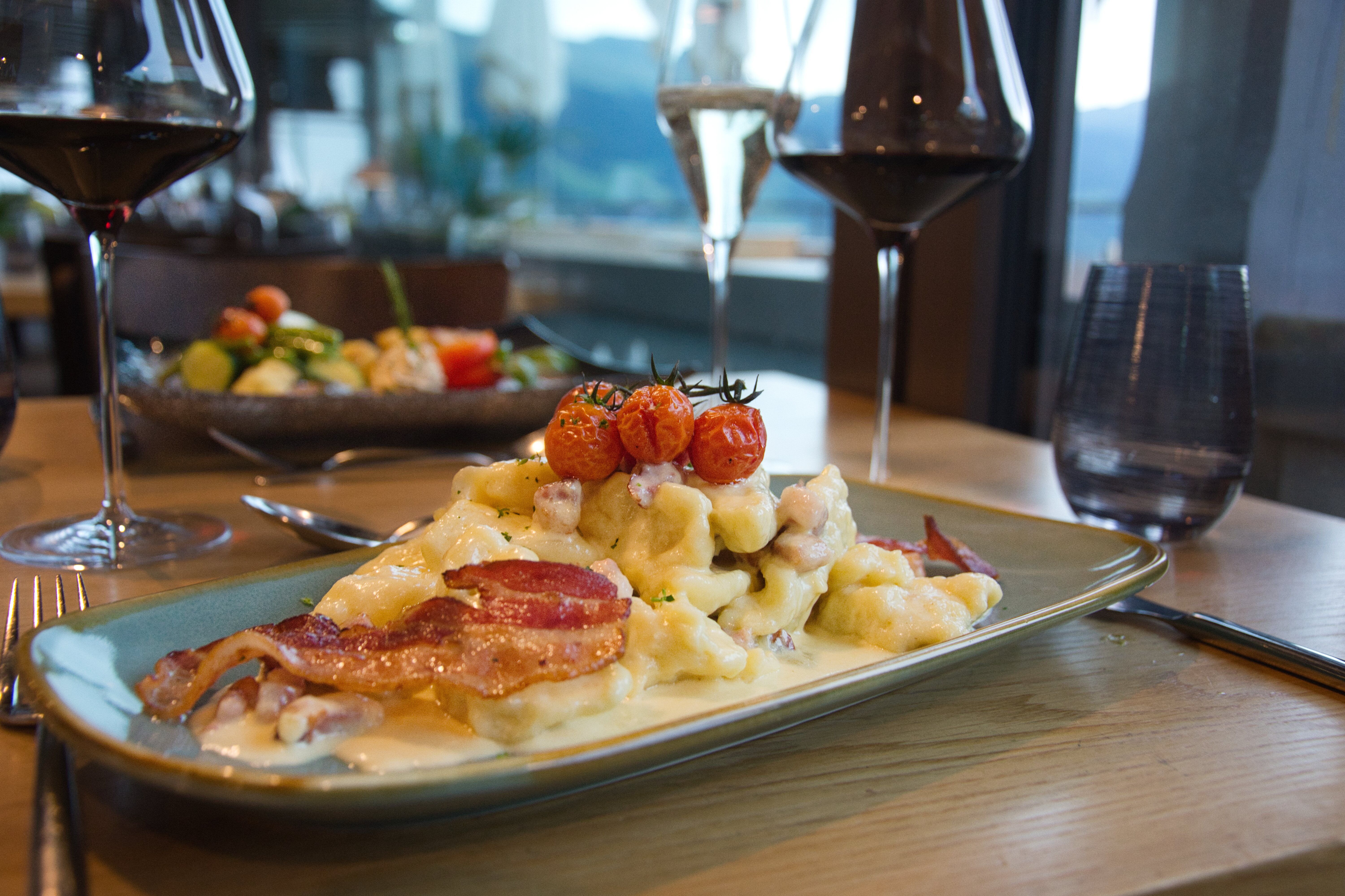 Mittagessen: Köstliches Kartoffelgericht mit Speck und Tomaten im Restaurant mit Bergblick.