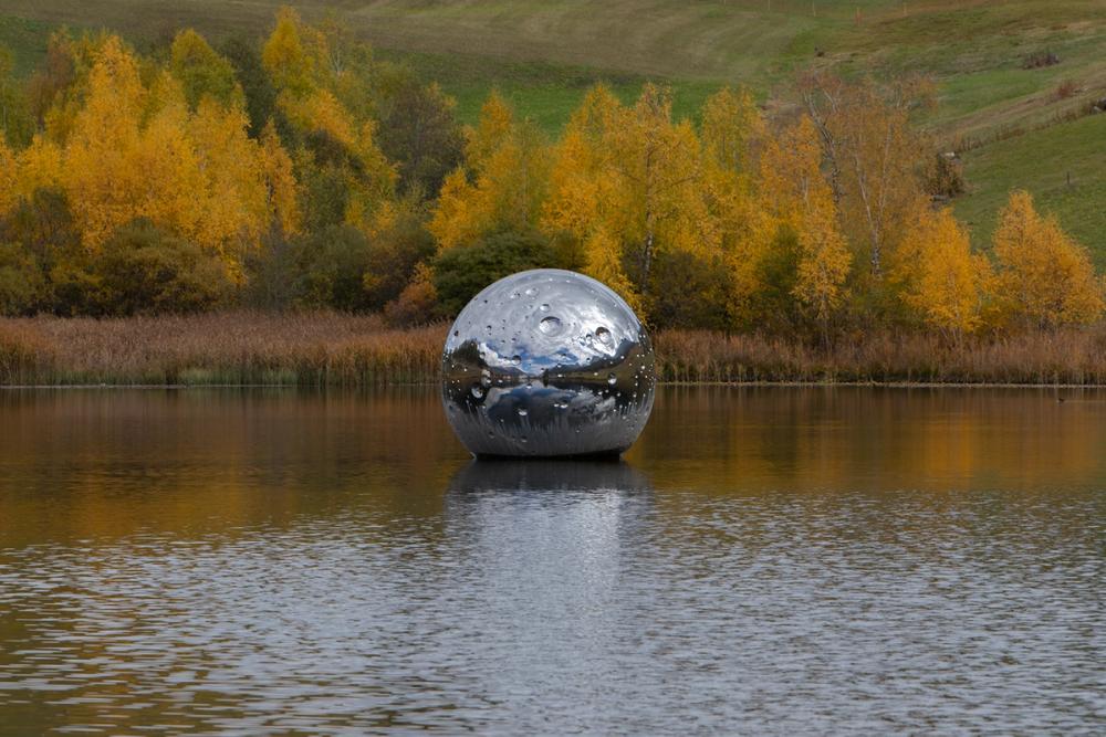 Měsíc se odráží v vodě, obklopený barevnými stromy na podzim, idylická přírodní scenérie.