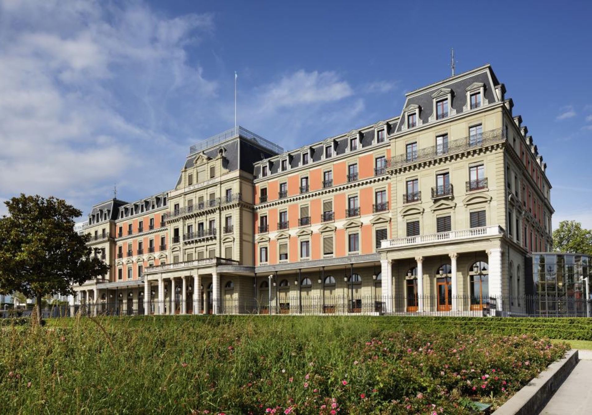 Explorial Γενεύη: Καγκελόσπιτο σε κομψό κτίριο στην πόλη, περιβαλλόμενο από όμορφ Green και λουλούδια.