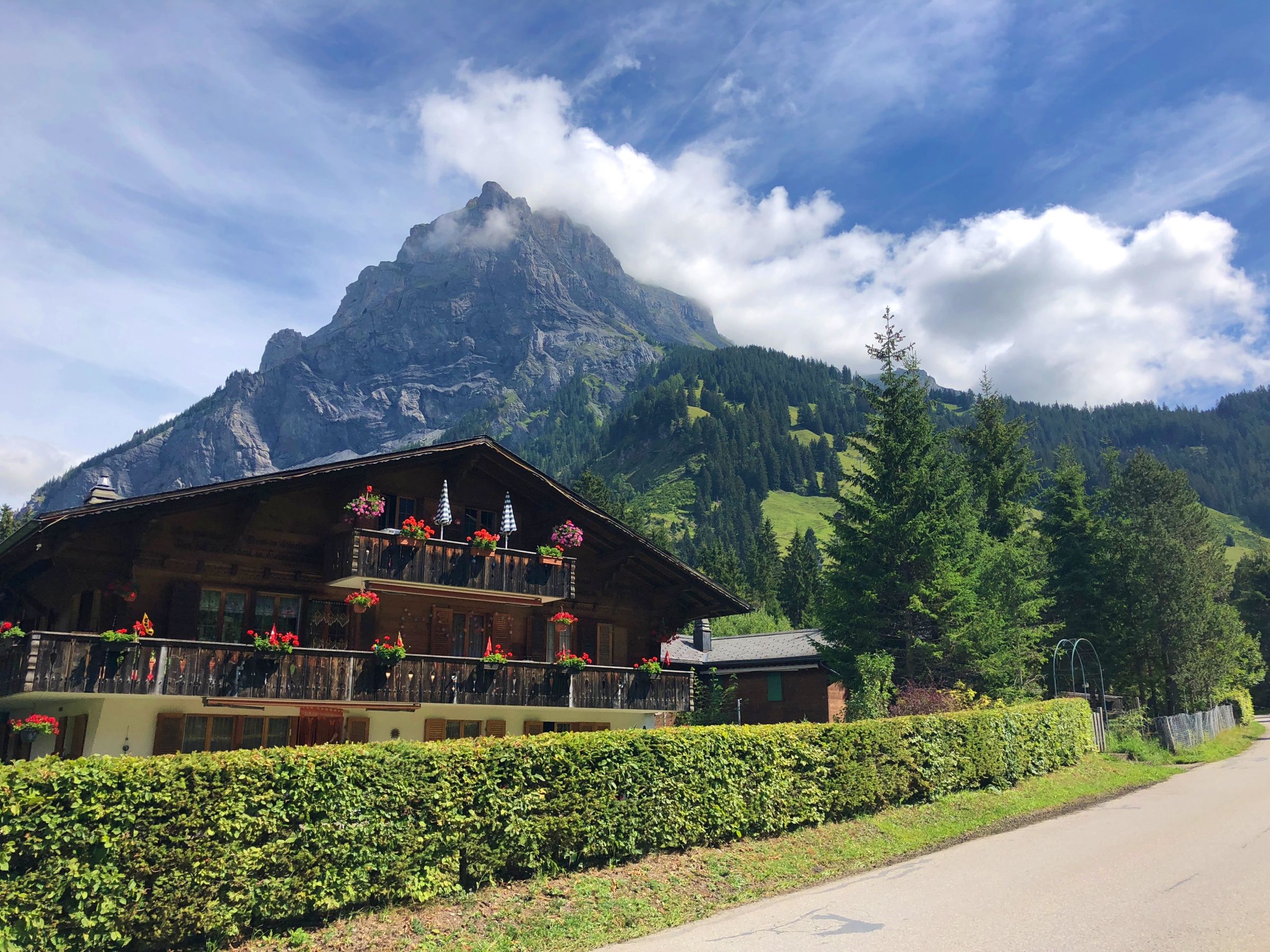 Oeschinensee s typickou chatou, horskou krajinou a modrou oblohou.
