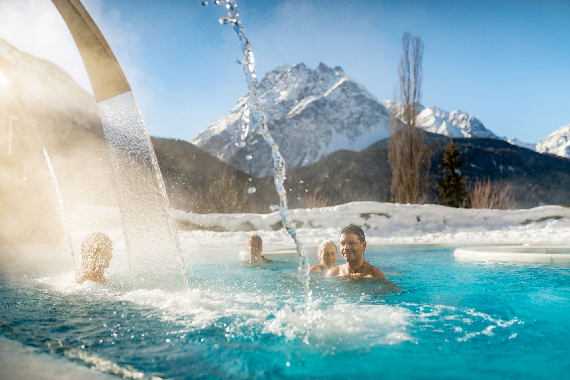 Utomhusbad i vinter i Scuol med snöklädda berg och avkopplande gäster.