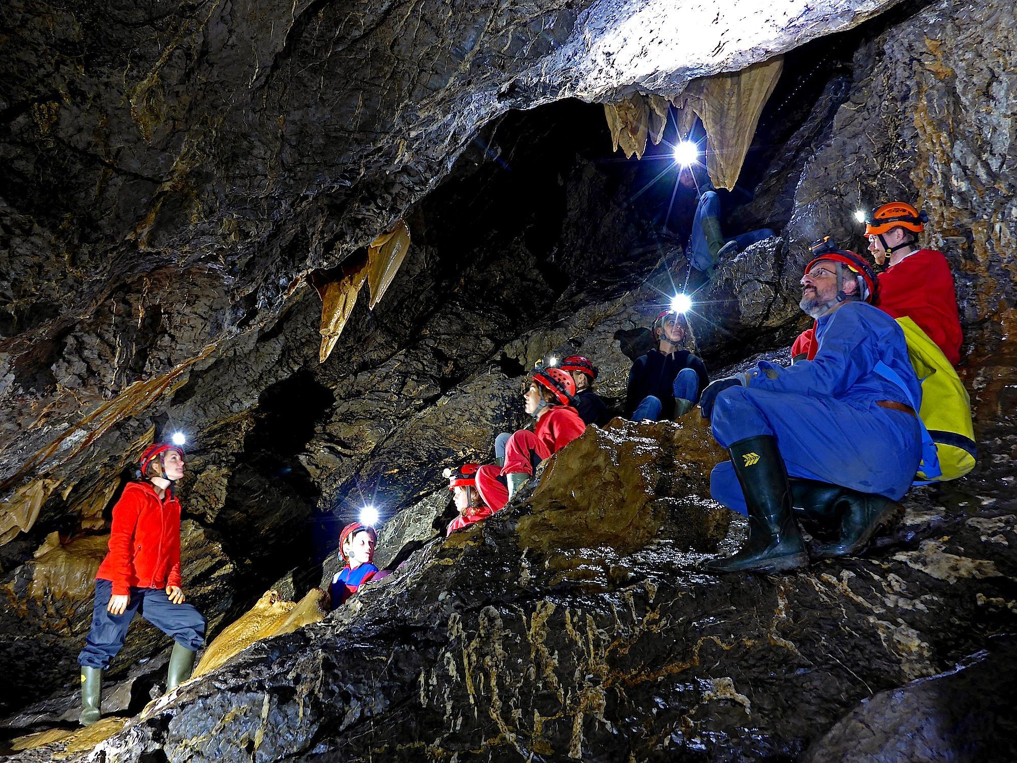 Recorrido de senderismo en cuevas con participantes en una cueva, linternas brillando