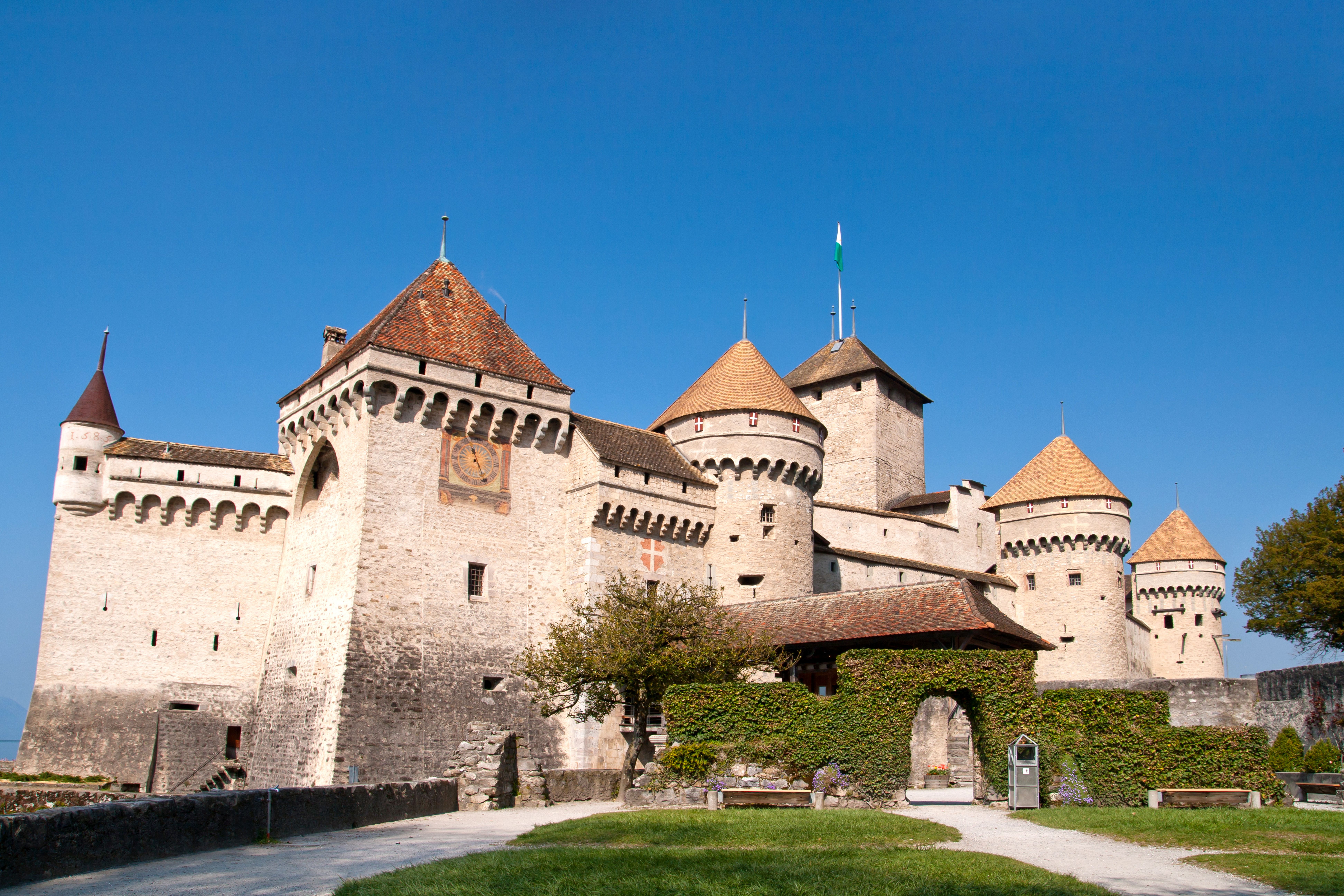 Chateau Chillon di Tasik Geneva dengan taman dan langit biru.