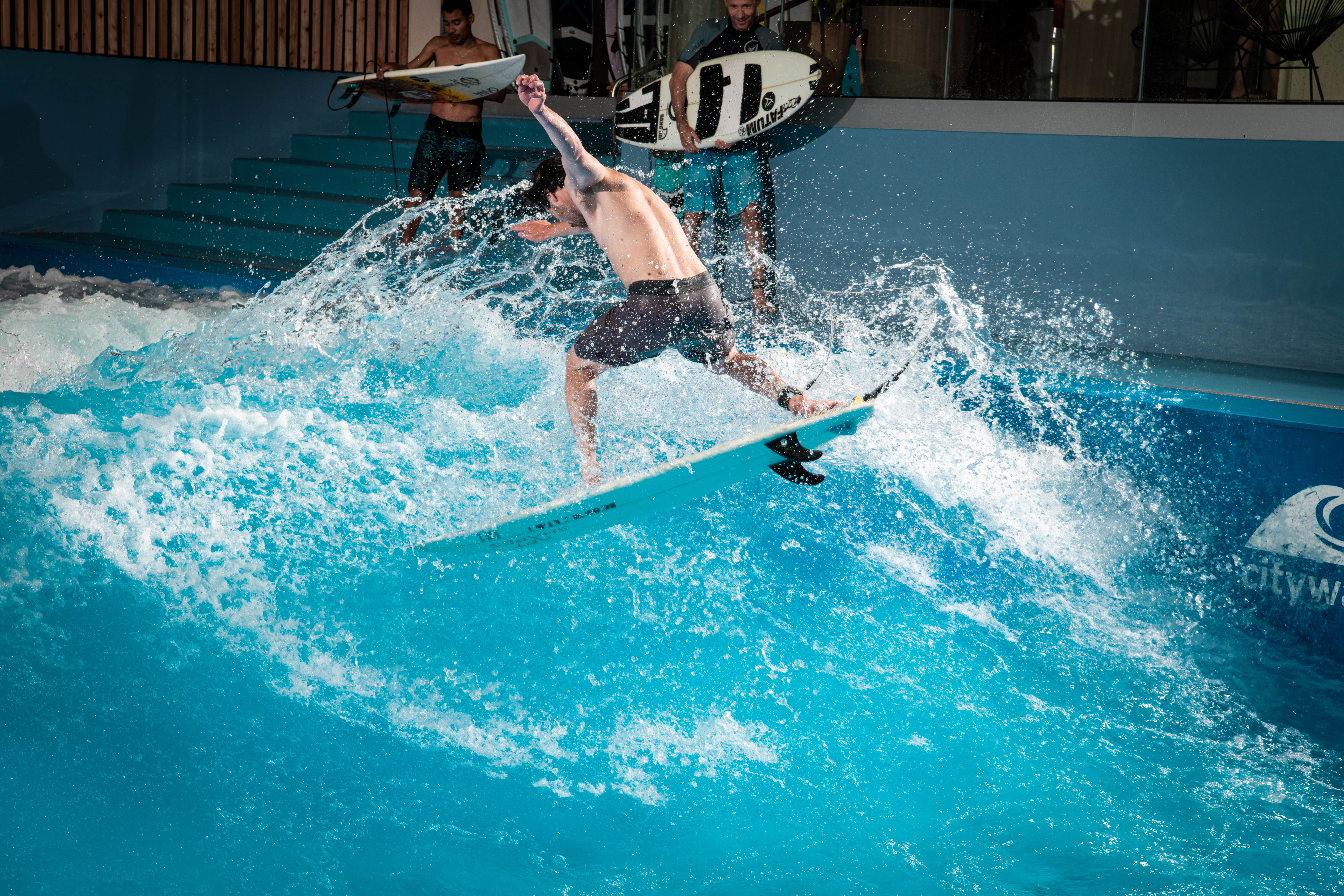 Oana Surf mentre fa surf in piscina, surfista salta sopra l'onda, acqua blu