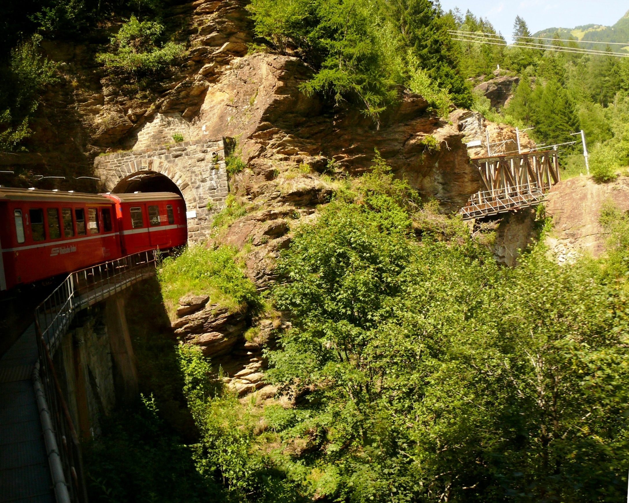 Rätisktåg: ett rött hjulhjulståg färdas genom gröna landskap i Alperna.
