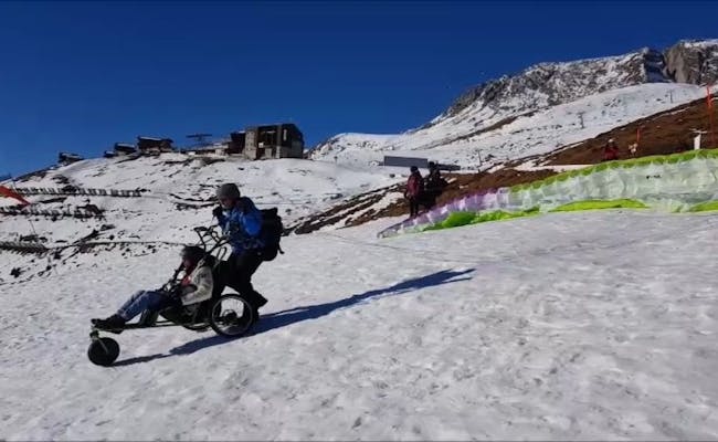 Volo in tandem con parapendio per persone in sedia a rotelle sulla neve con accompagnamento e parapendio colorato