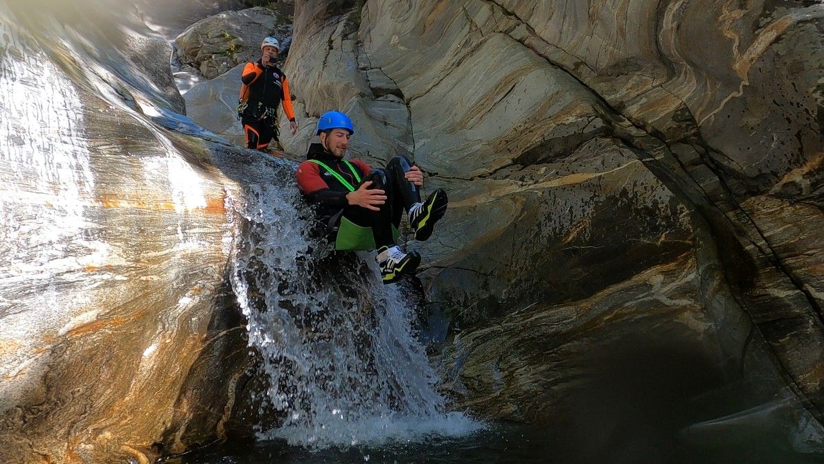 बोगेरा कैन्यन रपटिंग: व्यक्ति नदी के झरने पर फिसलता है, चट्टानों और पानी से घिरा हुआ