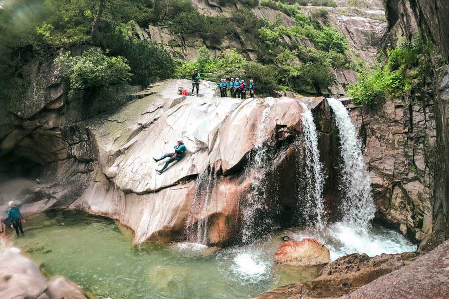 Sliding Canyoning Grimsel, participants slide over rocks into a waterfall, surrounded by nature