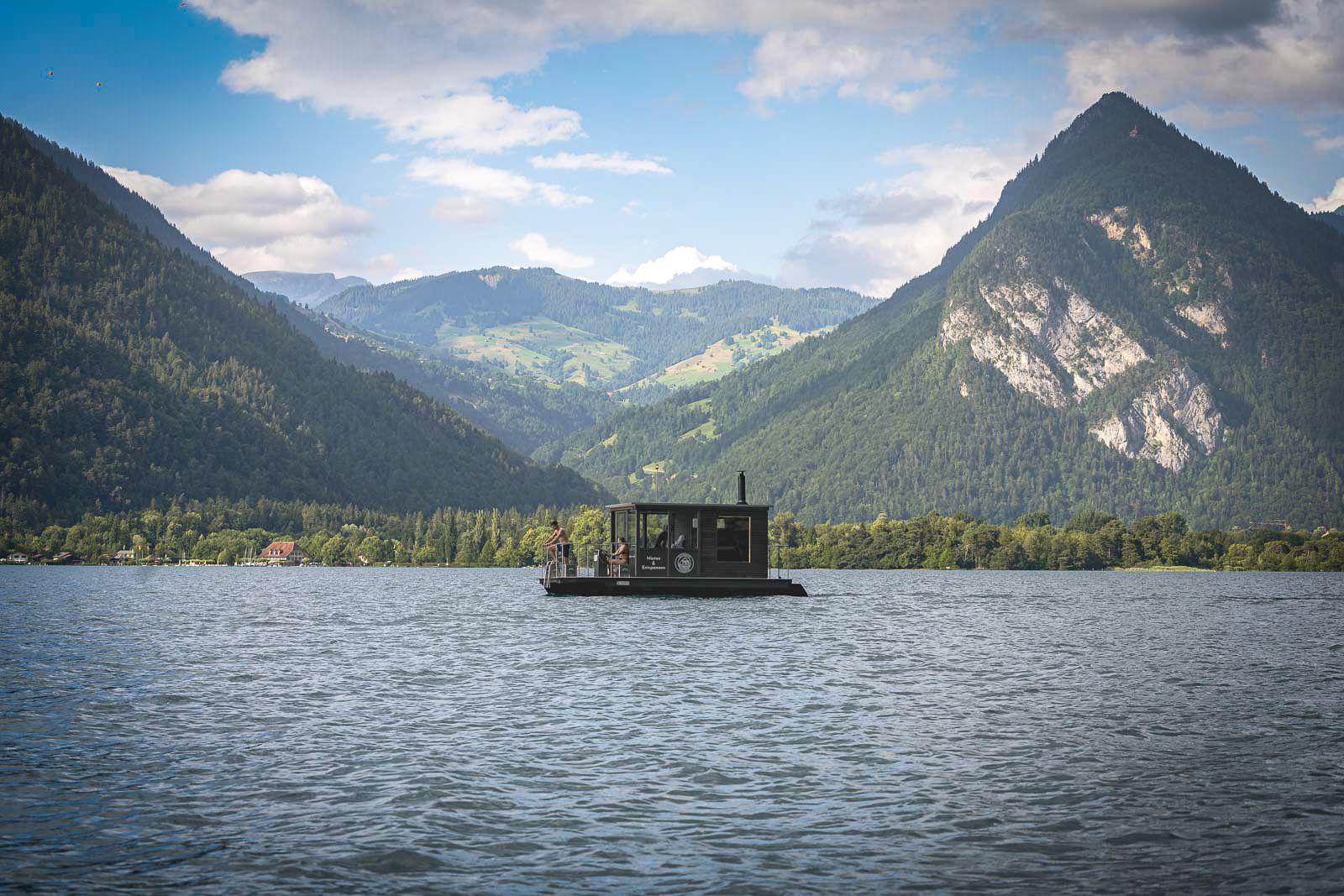 Barcă cu saună pe lac, înconjurată de munți impunători în natură, perfectă pentru wellness și relaxare.