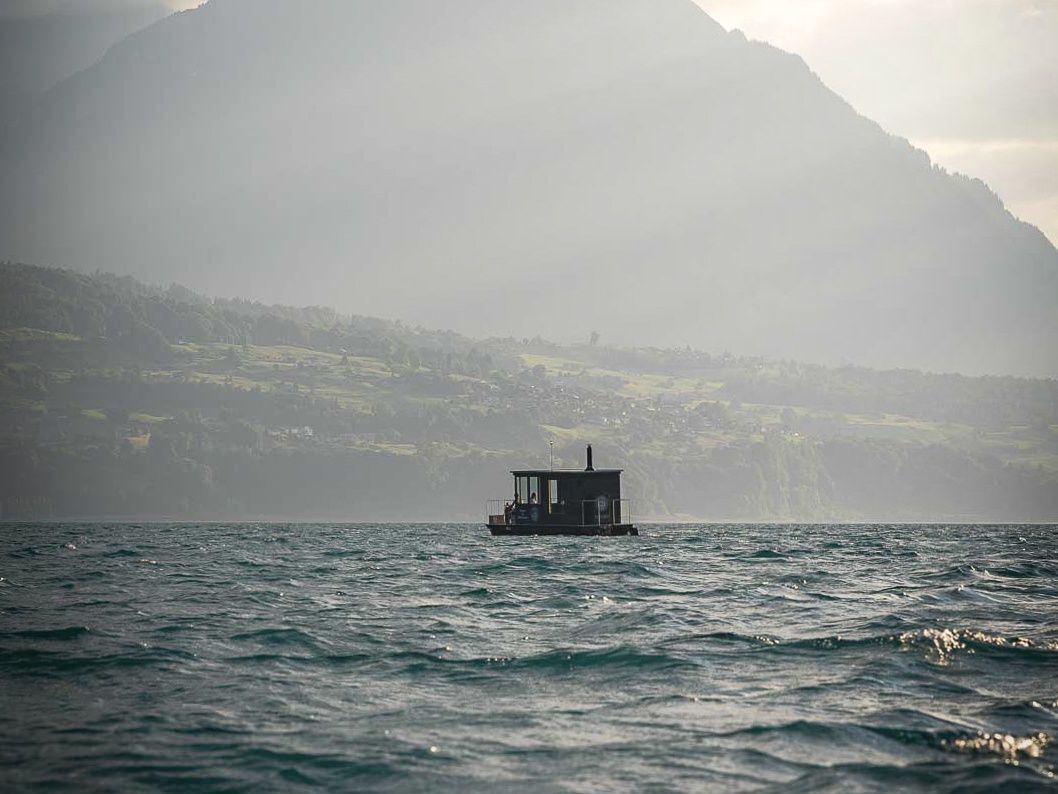 Plimbare cu saună pe apă, cu vedere către munți, într-un mediu liniștit lângă lac.