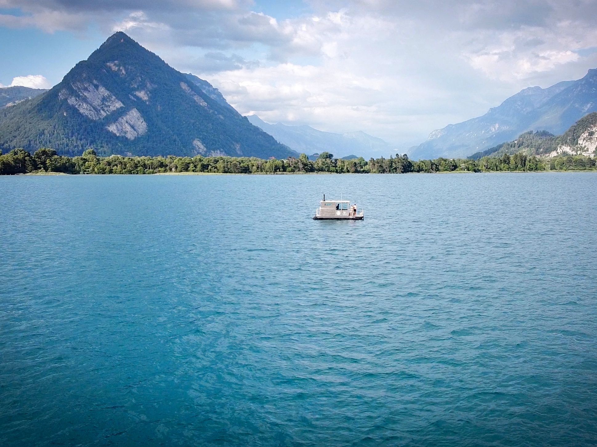 Barca de saună pe lac, înconjurată de munți și natură, perfect pentru relaxare vara.
