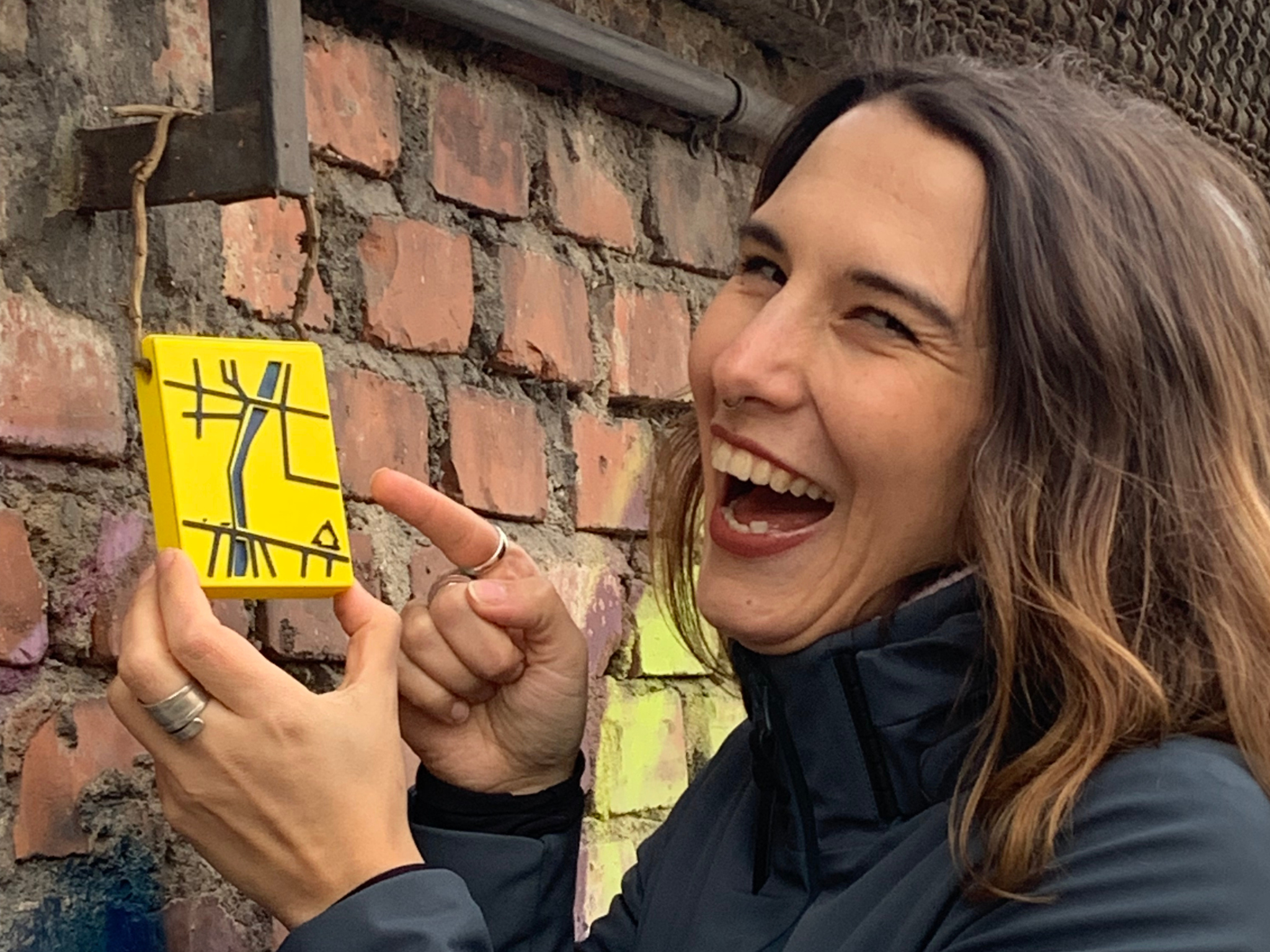 Sato Code: Frau zeigt kreatives Straßenkunstwerk in urbaner Umgebung, Kunst, Team, Abenteuer.