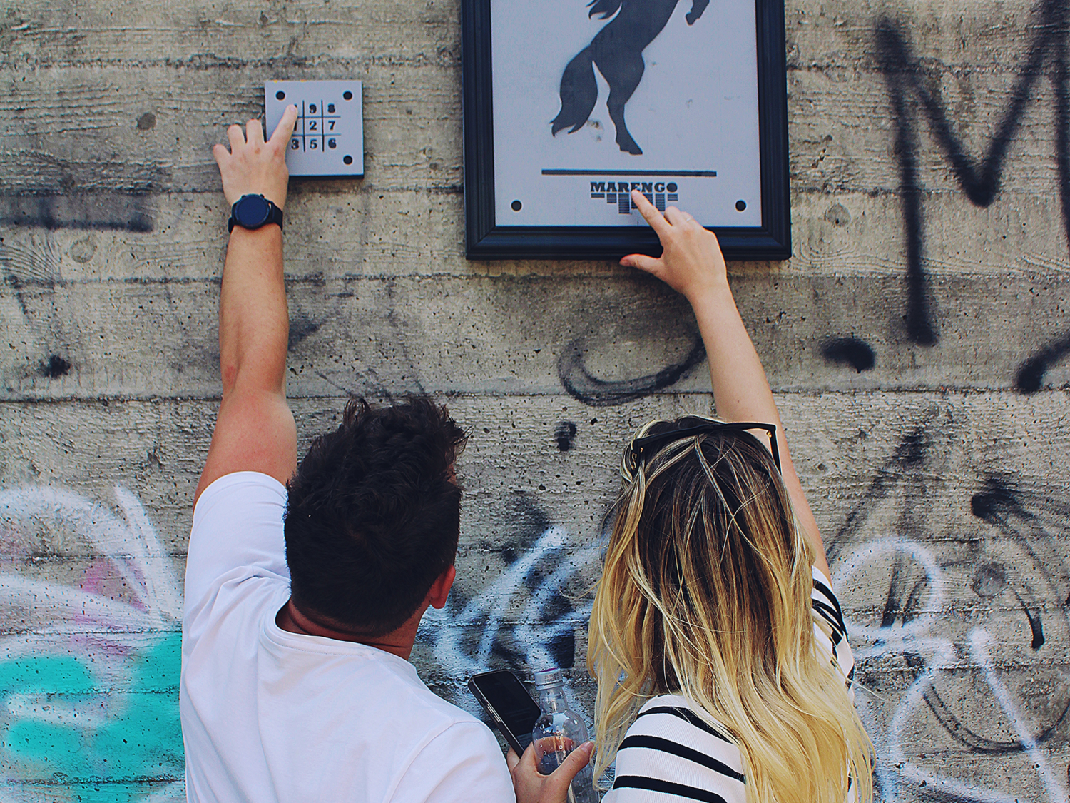 Sato Code: zwei Personen betrachten ein Graffiti an einer Wand in einer urbanen Umgebung.