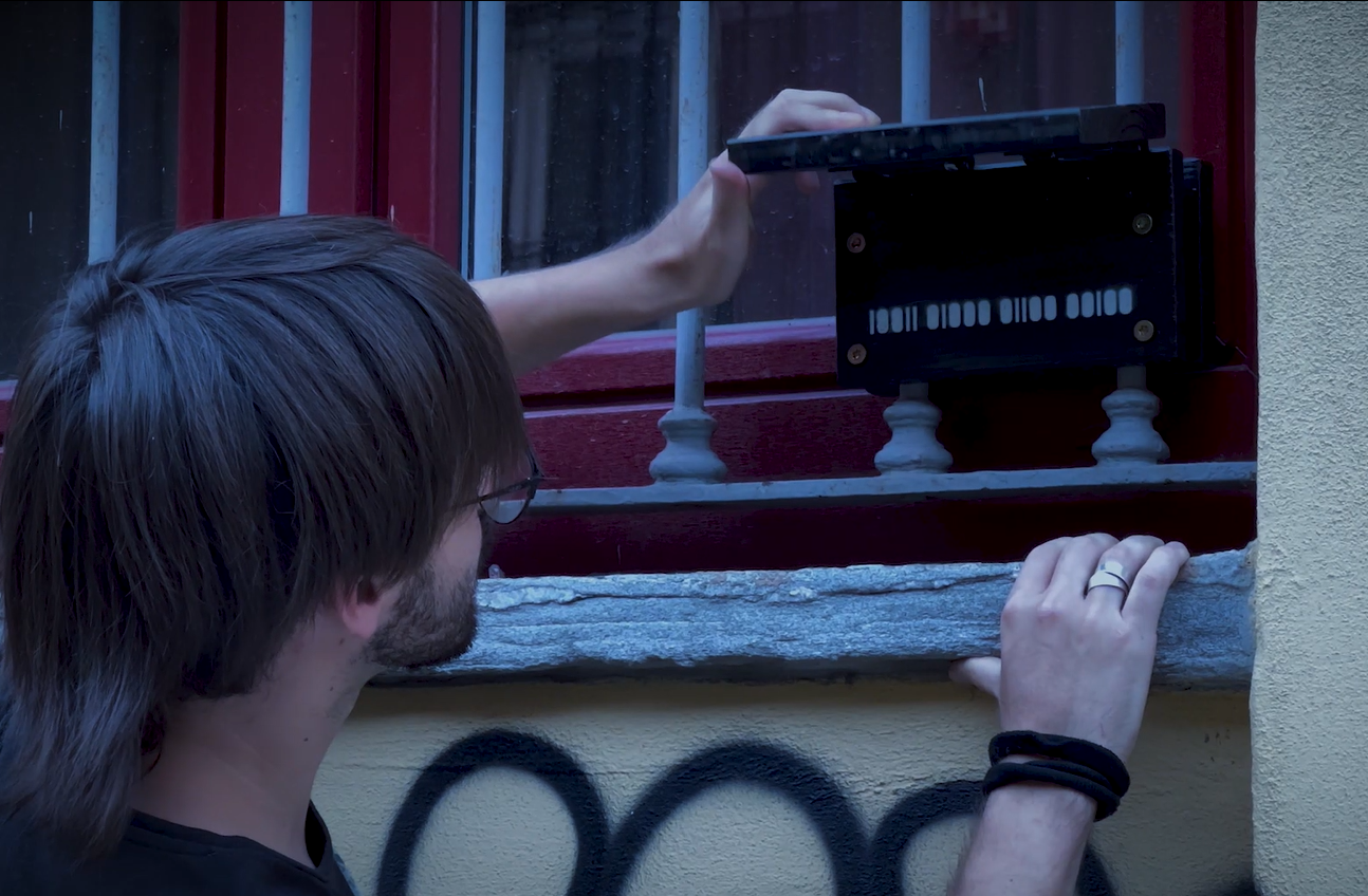 सतो कोड: शहर में क्रिएटिव इंस्टॉलेशन के साथ खिड़की पर युवा पुरुष, शहरी कला, रचनात्मकता