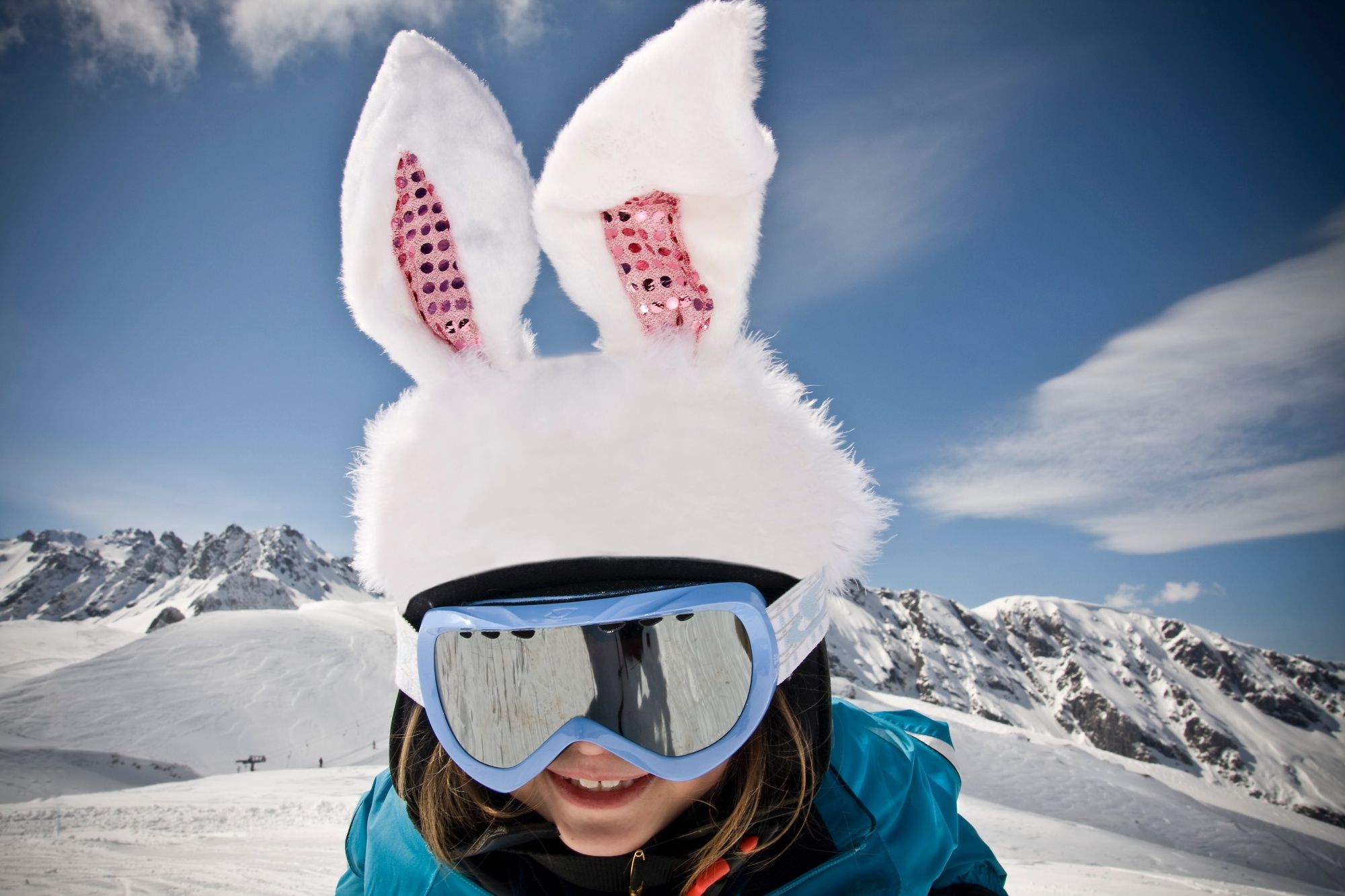 Biały królik: dziecko w goglach narciarskich i uszach zająca zimą na Pizol, na tle pokrytych śniegiem gór.