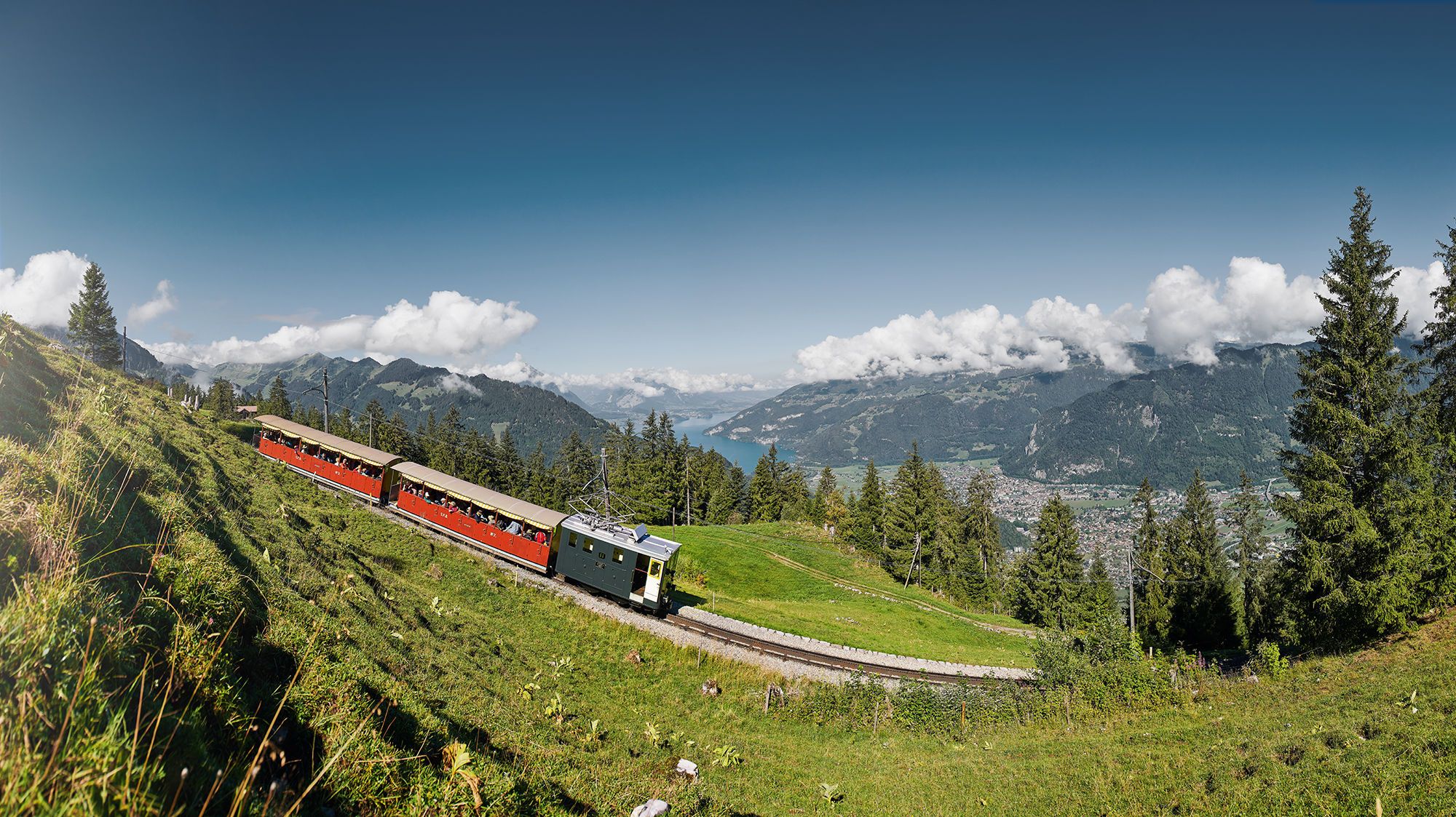 Schynige Platte Bahn fährt durch eine grüne Berglandschaft mit See