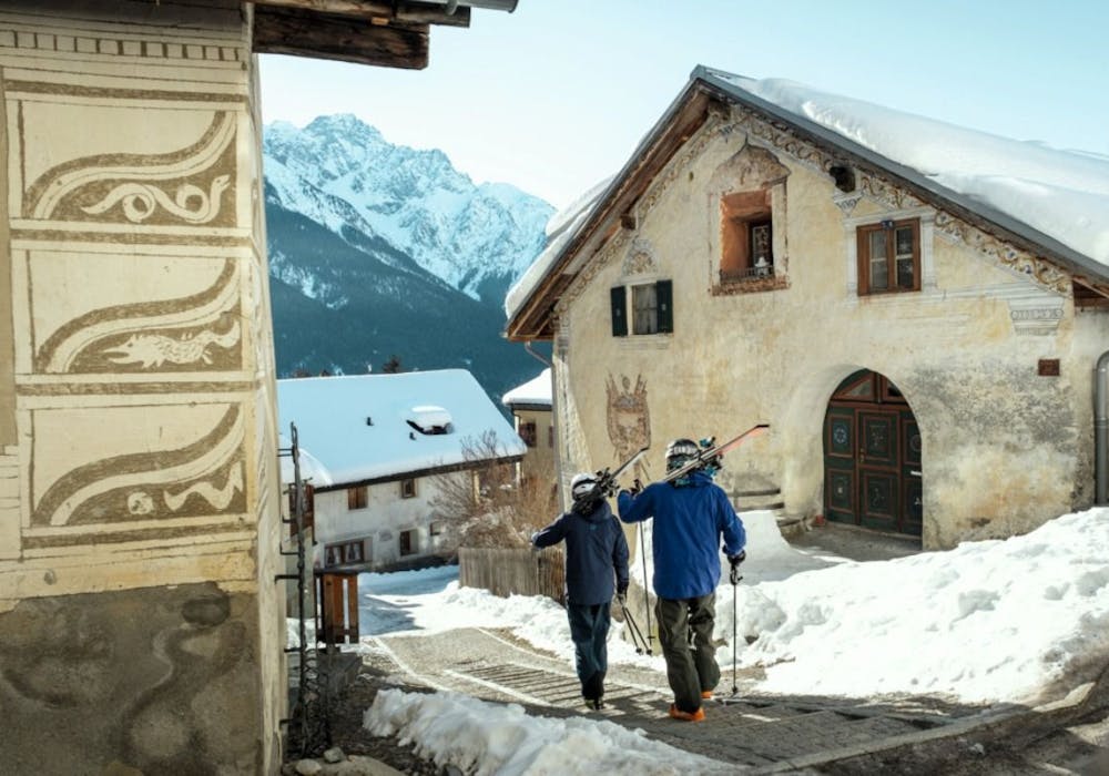 Esquiadores en Scuol se mueven por calles nevadas hacia su próximo destino.