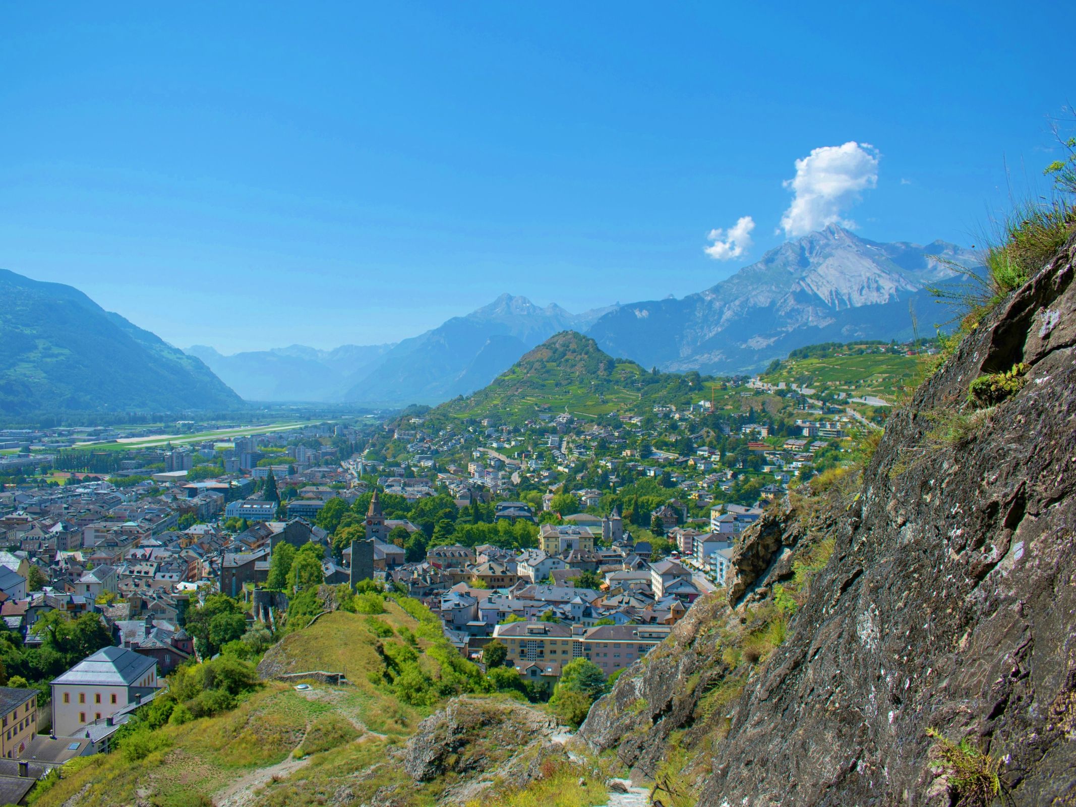 Sion: Pandangan ke kota dengan gunung, rumah yang indah, dan alam semula jadi di musim panas.