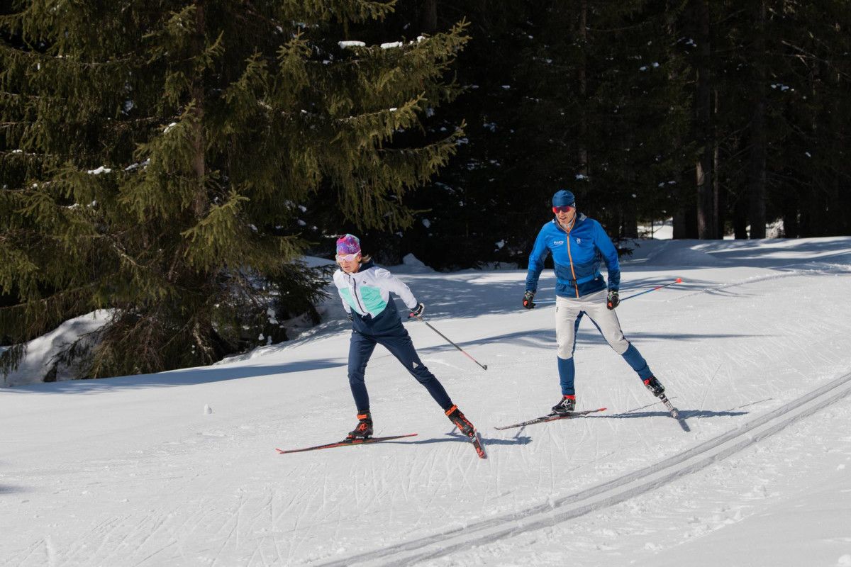 Cours privé de ski de fond skating à Davos avec deux skieurs dans la neige et des arbres.