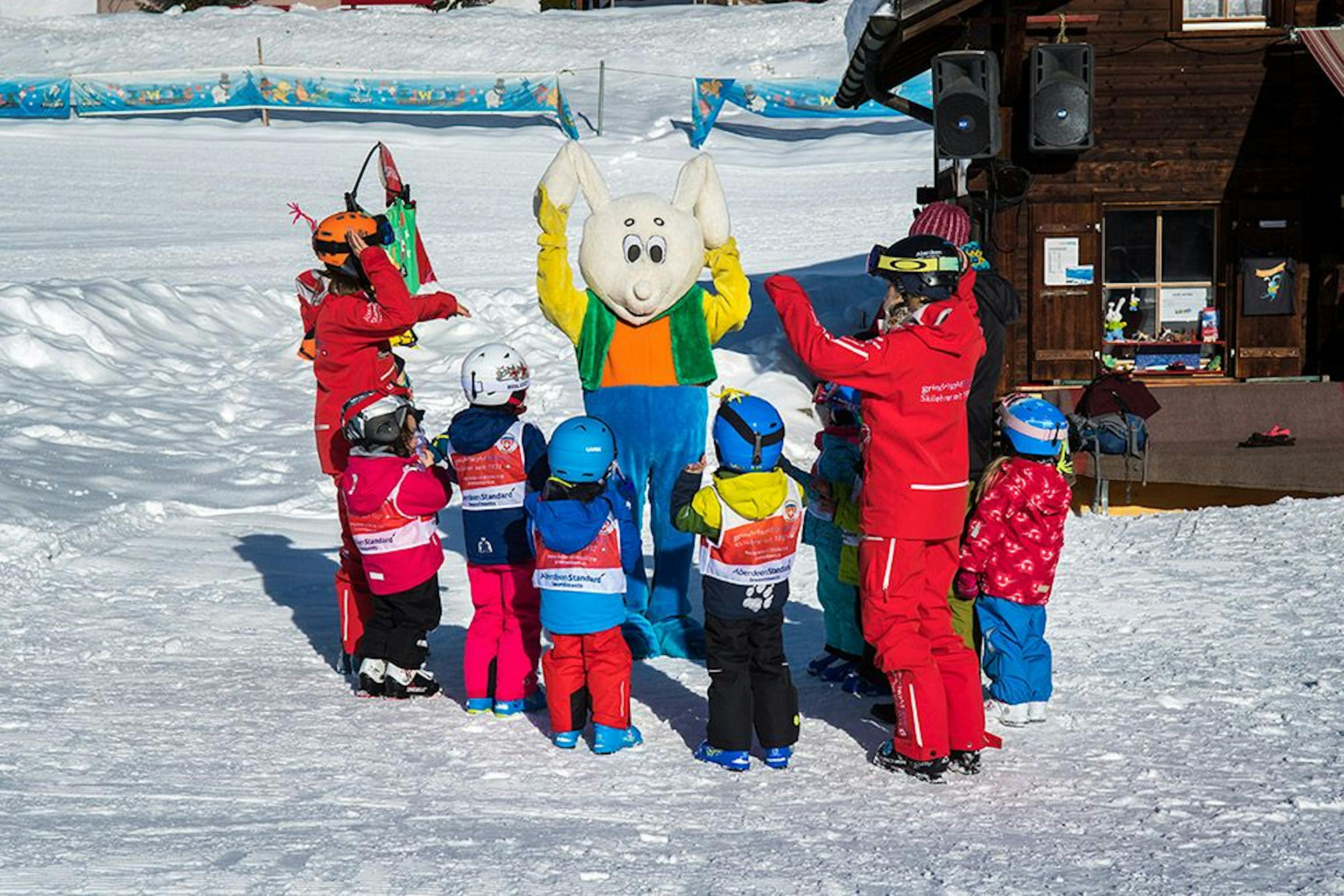 Groep ski-les voor kinderen in Grindelwald met een kleurrijk mascotte en blije deelnemers.