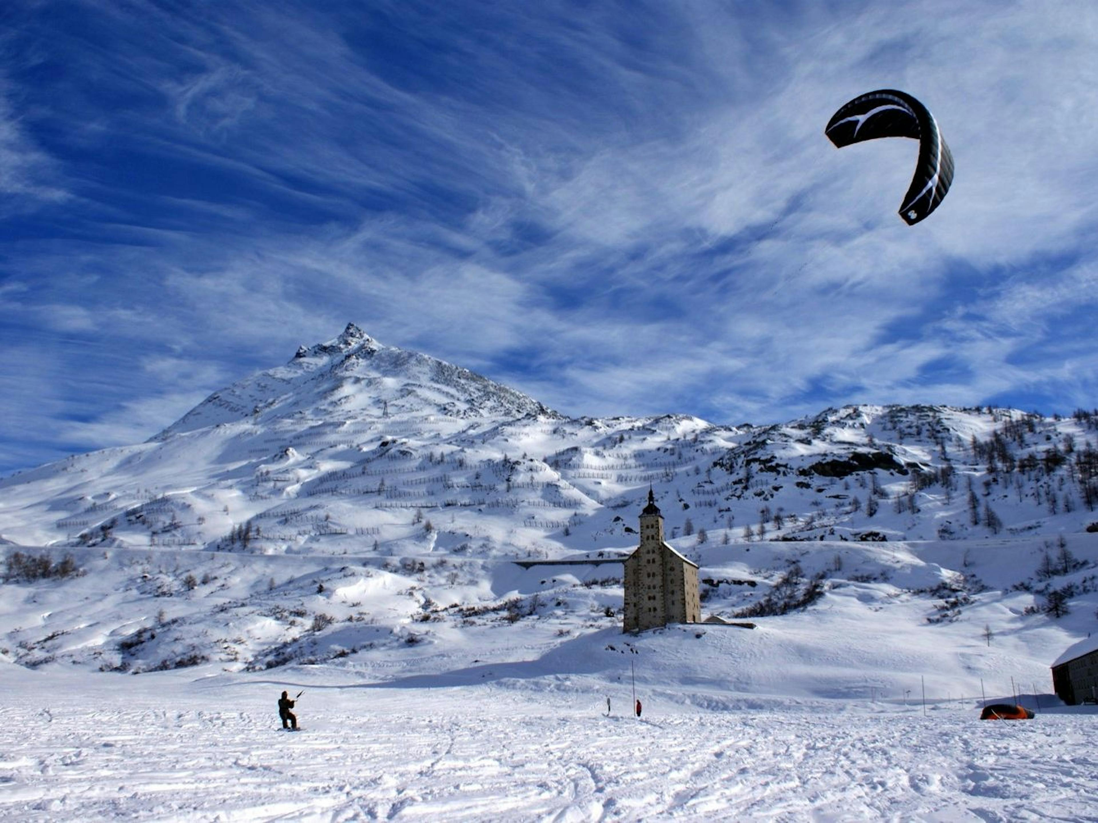 Corso di Snowkite Simplon con volo con il kite sulla neve e paesaggi montani.