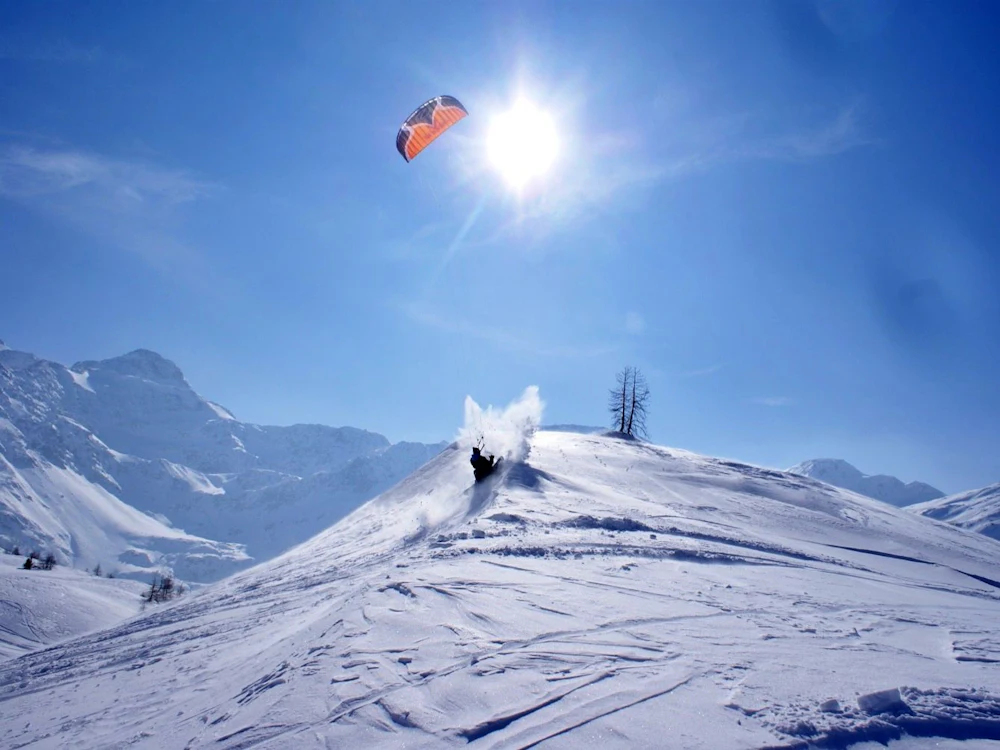 Snowkite Simplon: A kiter rides over the snowy slope in the sunshine.